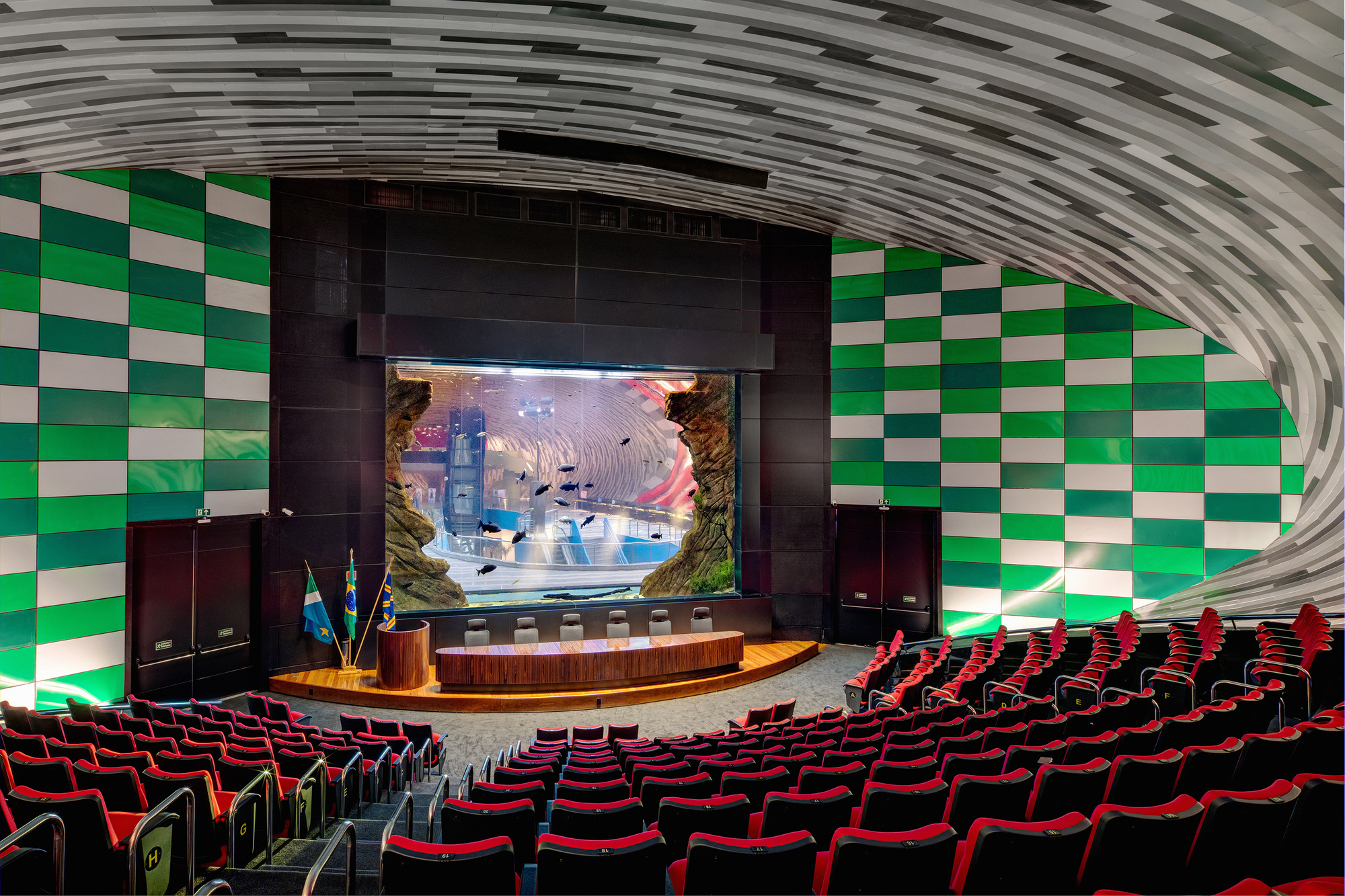 Auditorium stage framed by green checkered tile walls beneath a ribbed grey vaulted ceiling