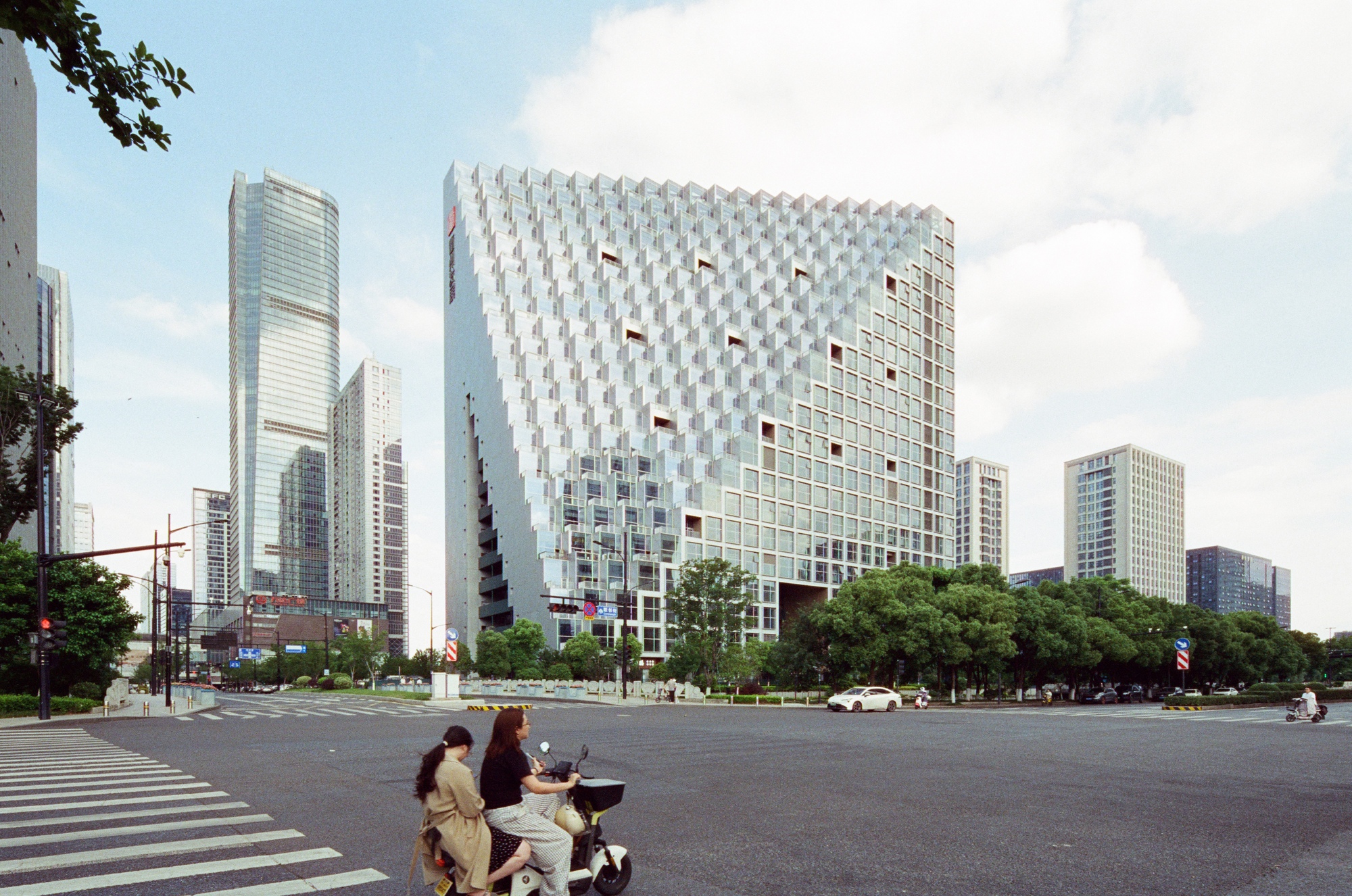Street view of the textured facade with recessed windows and a motorcyclist crossing the intersection