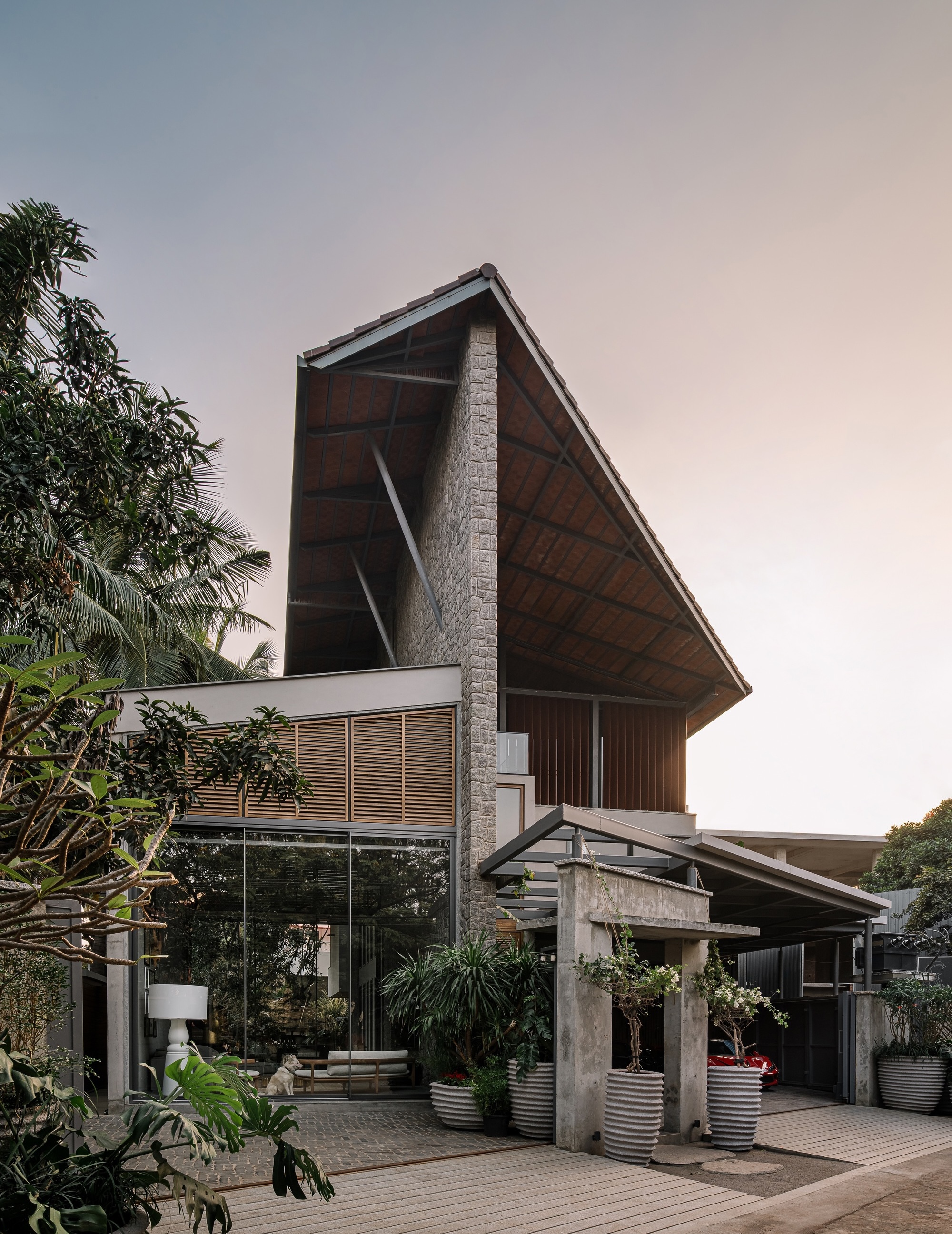 Angled timber roof with exposed structure rising above a wooden deck surrounded by tropical palms