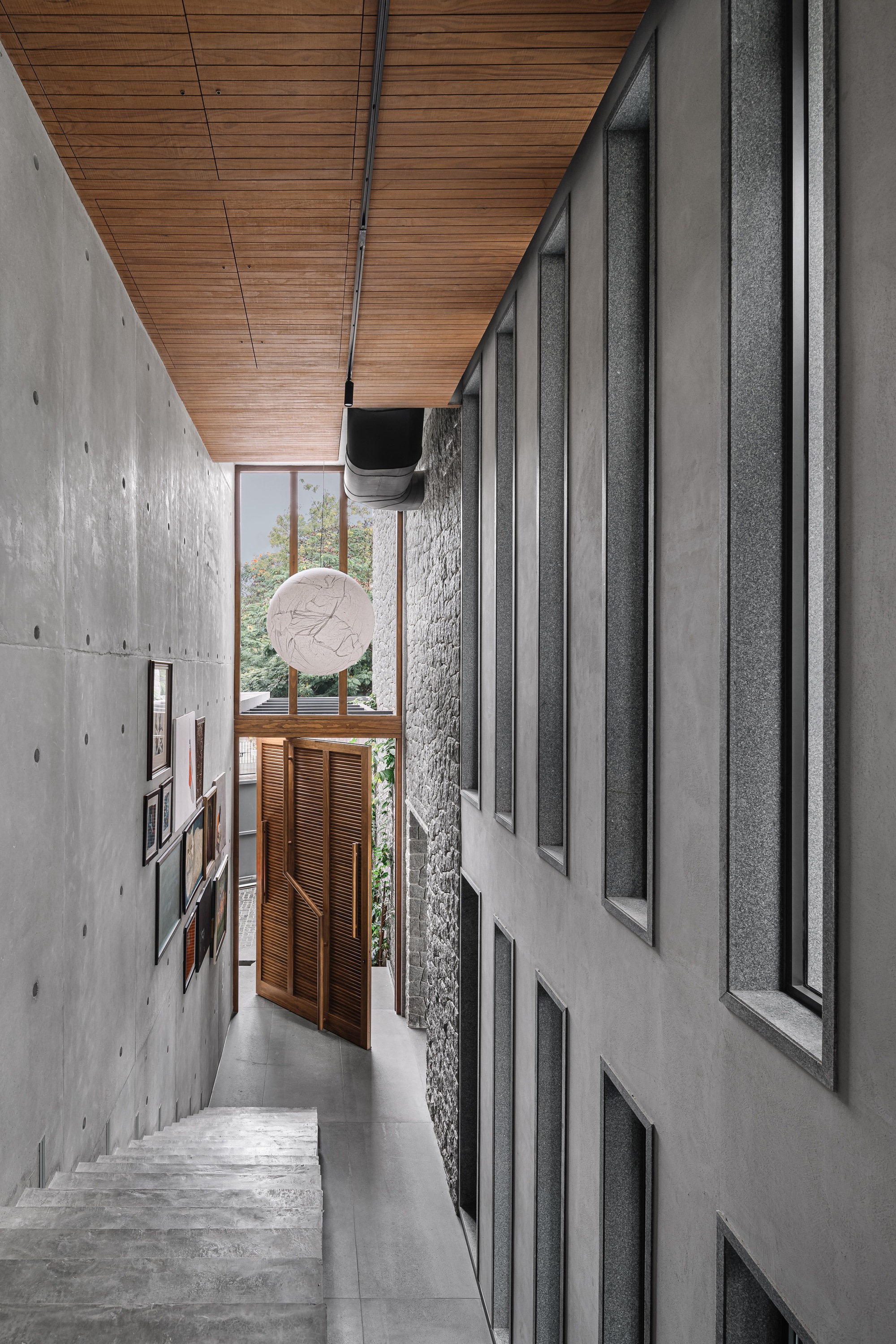 Narrow corridor with board-formed concrete walls, timber ceiling, and stairs descending toward wooden screens