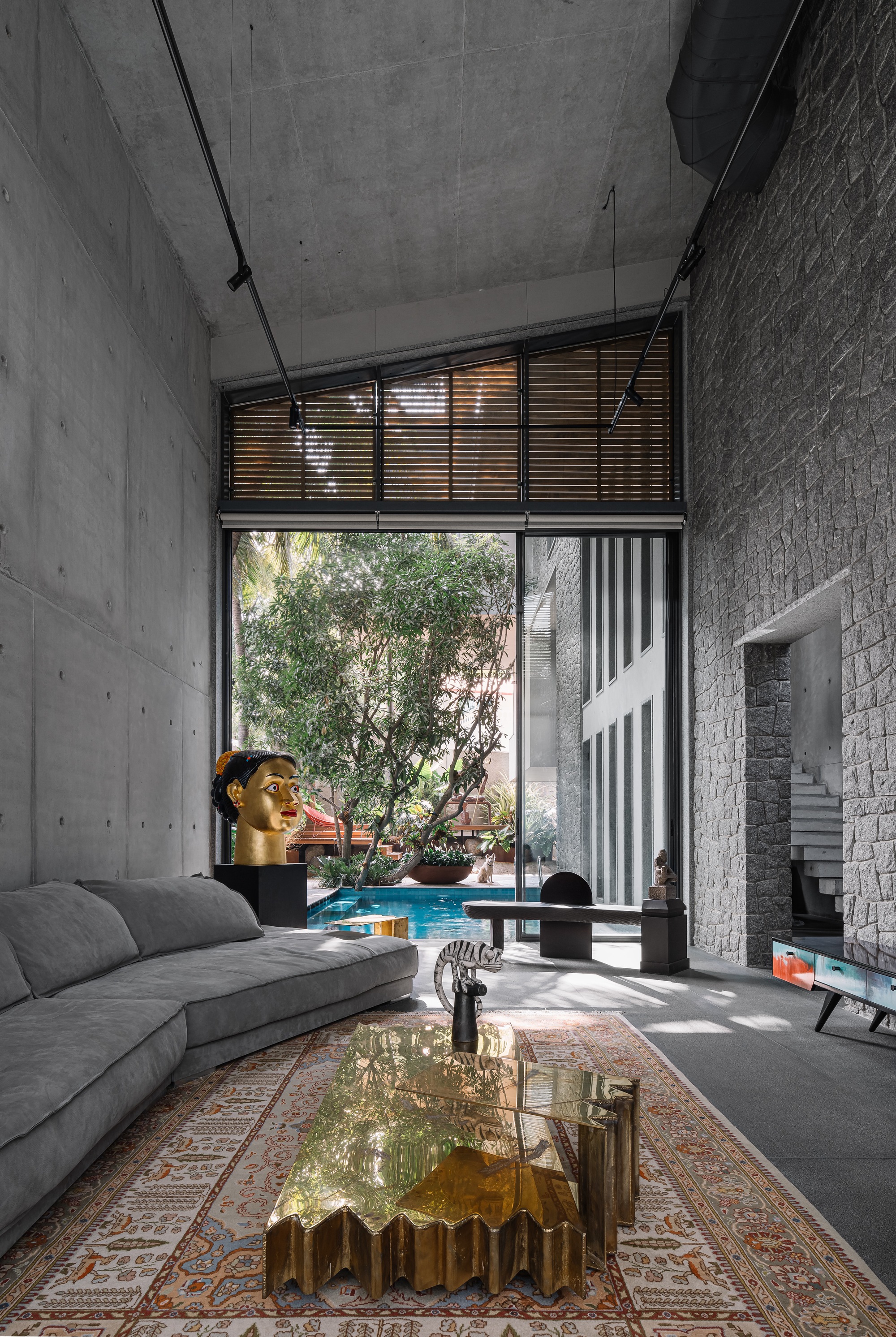 Double-height living room with concrete walls, slatted clerestory windows, and view to courtyard trees