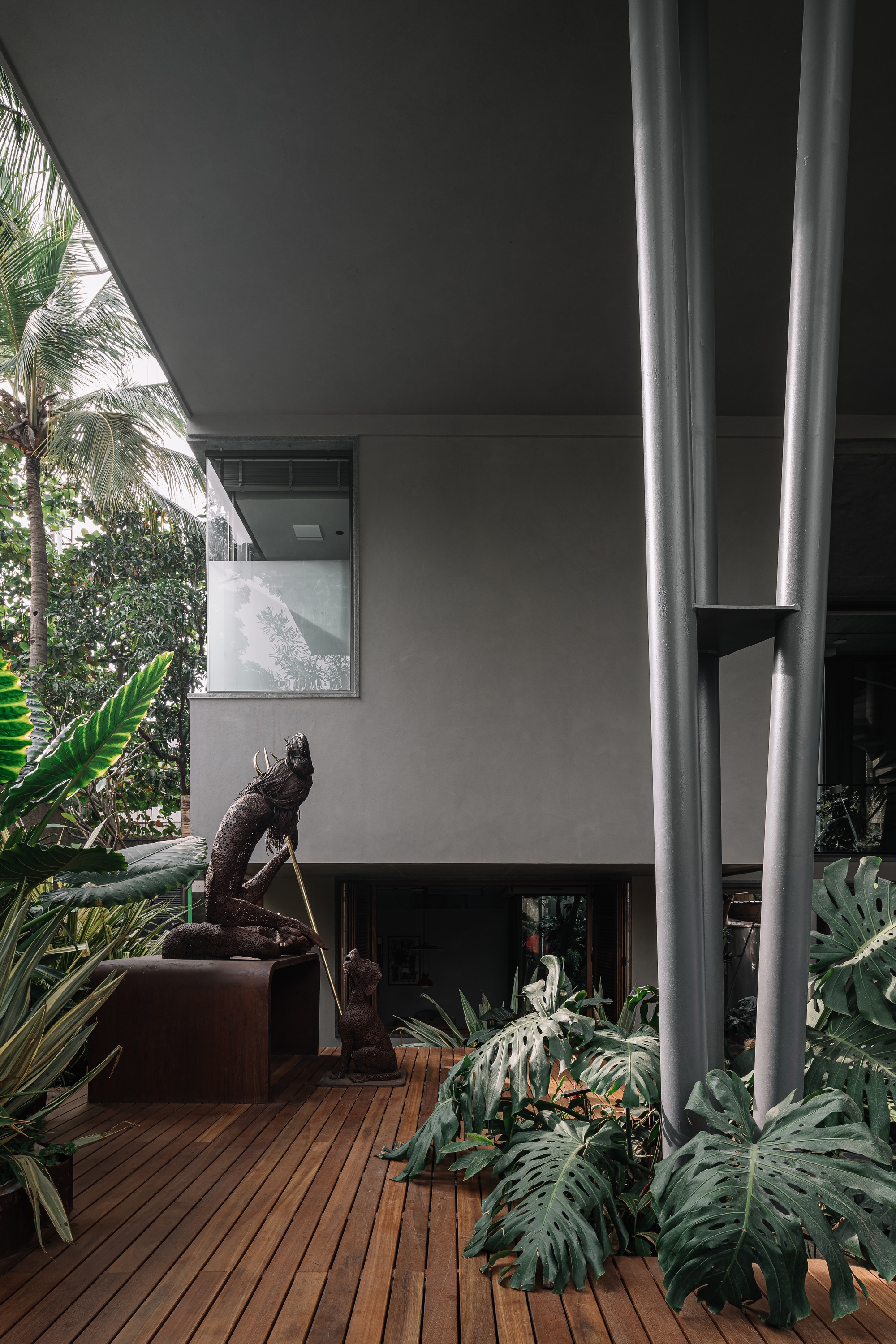 Covered terrace with timber decking, steel columns, tropical plantings and sculpture beneath exposed concrete soffit