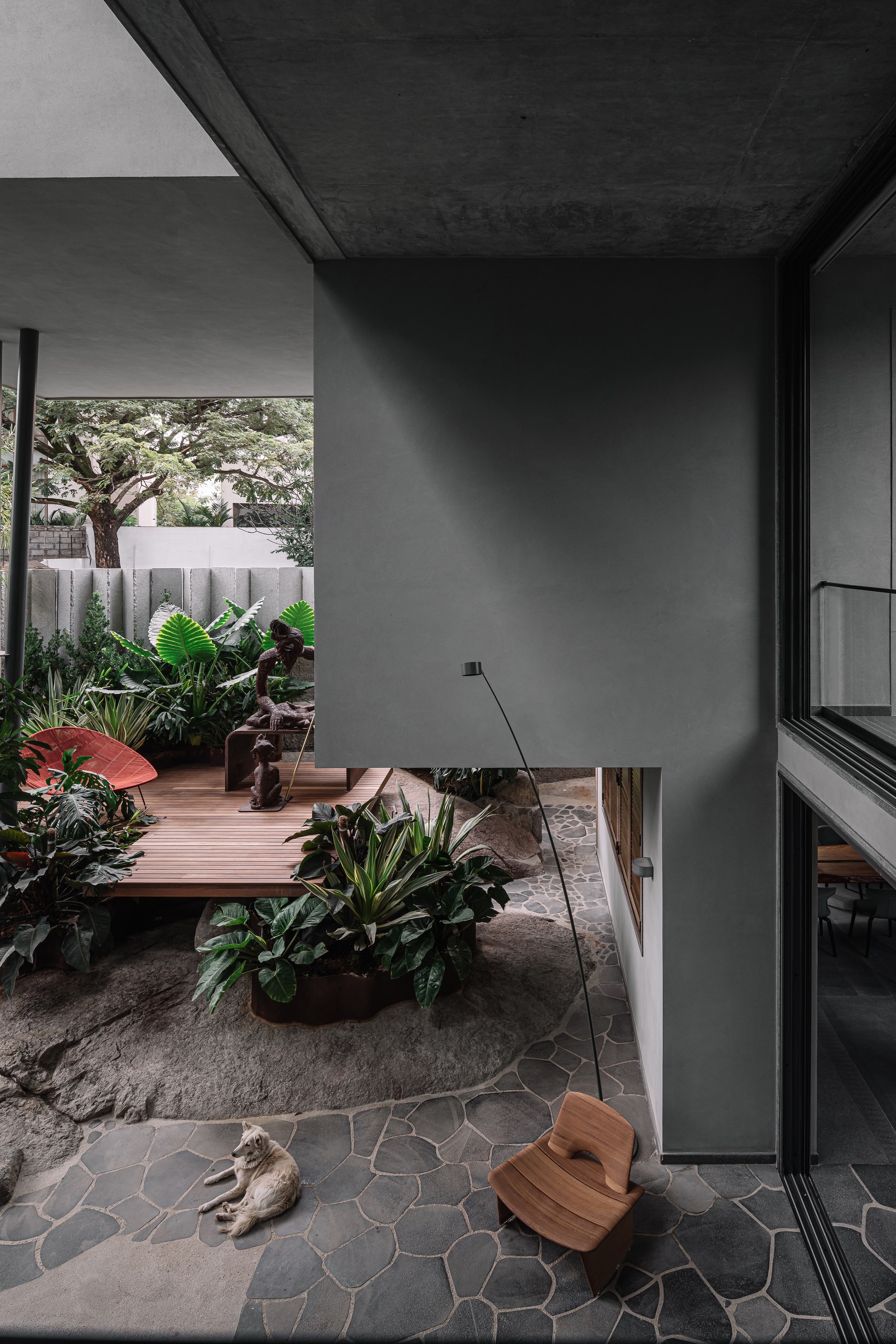 Interior view through glazed opening to courtyard with timber platform, potted plants and irregular stone paving