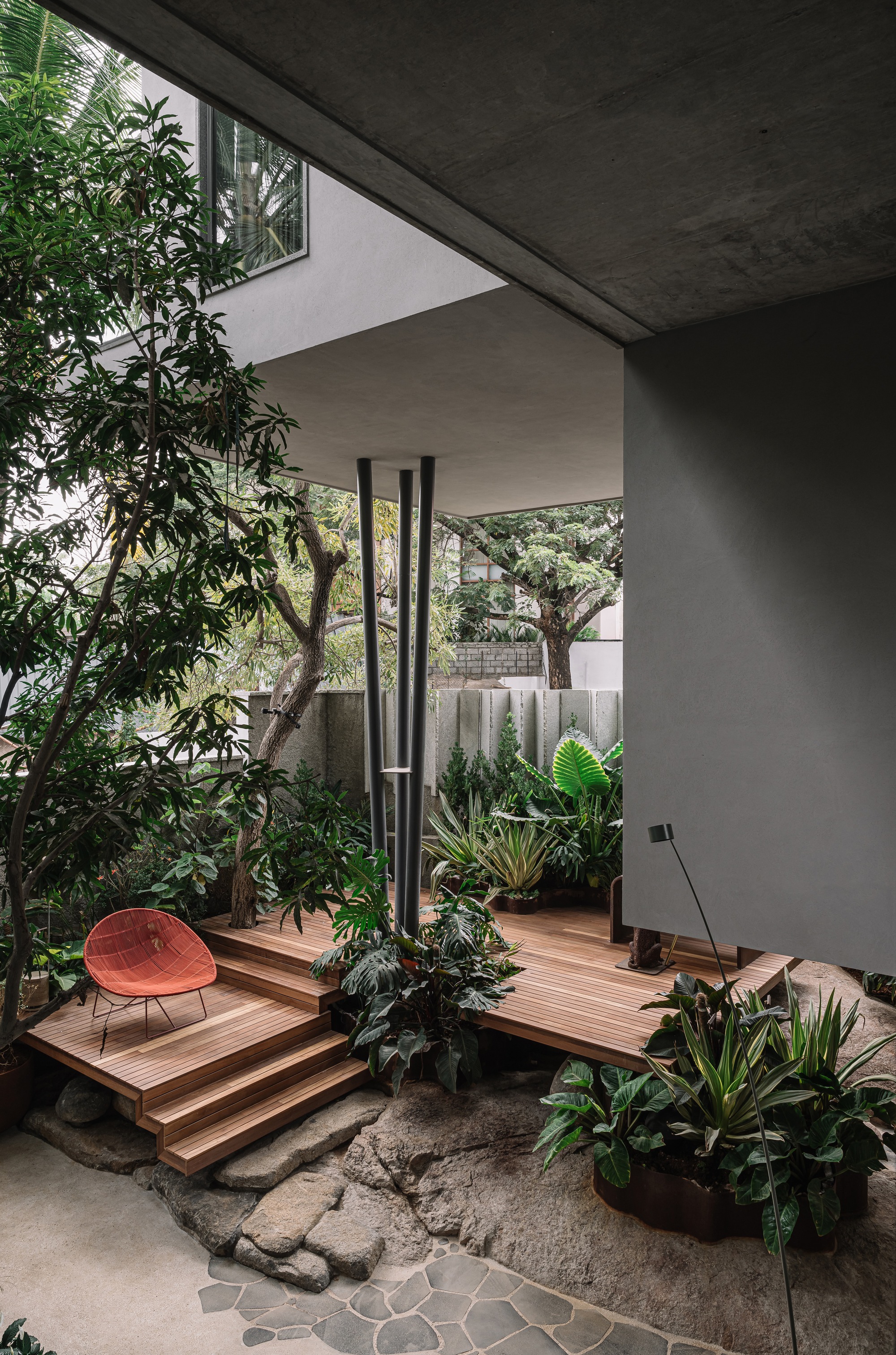 View through concrete frame to timber stair platform with steel columns, surrounded by planted garden beds and trees