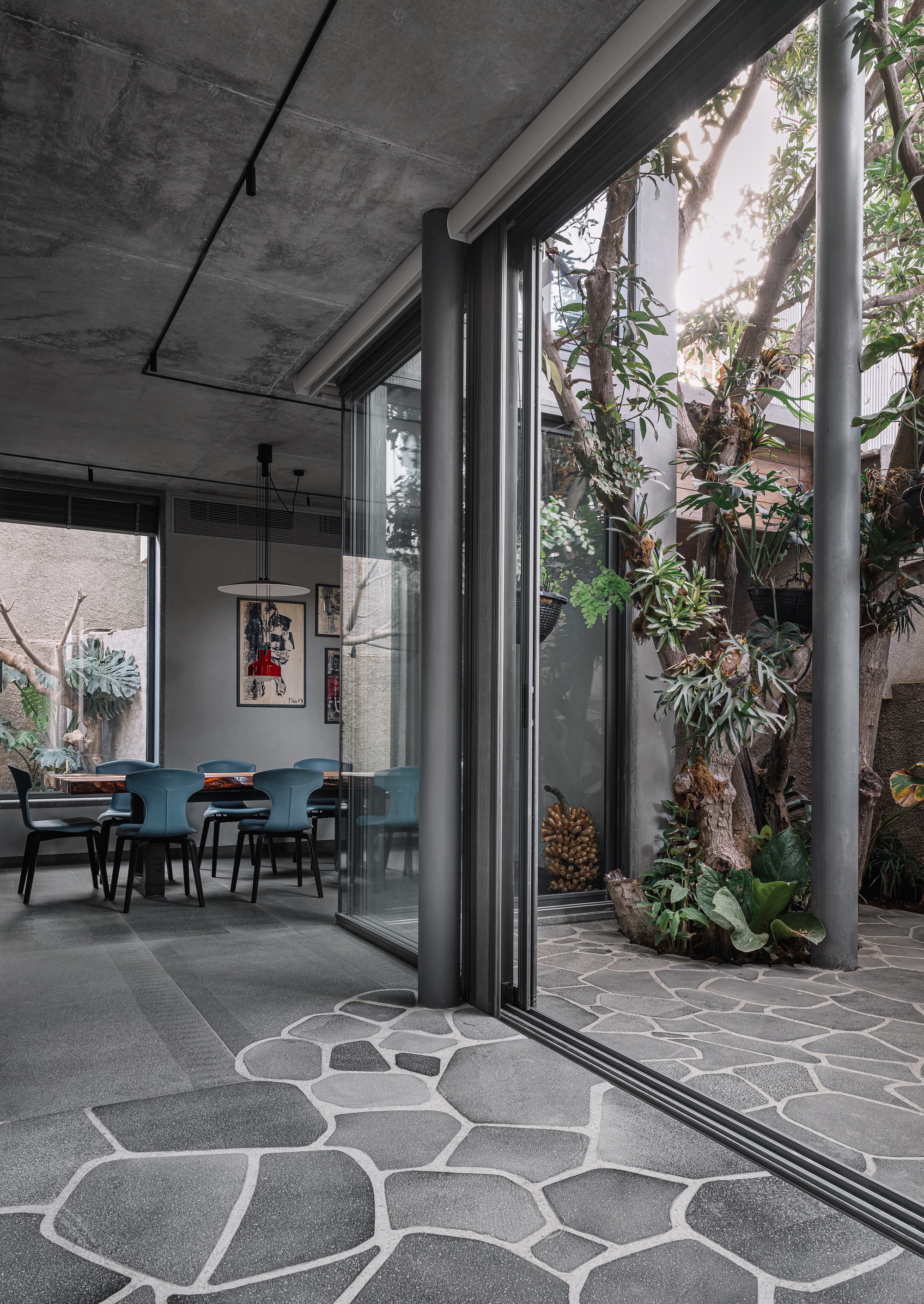 Fully open sliding glass doors connecting dining room to stone-paved courtyard with tropical plantings at threshold