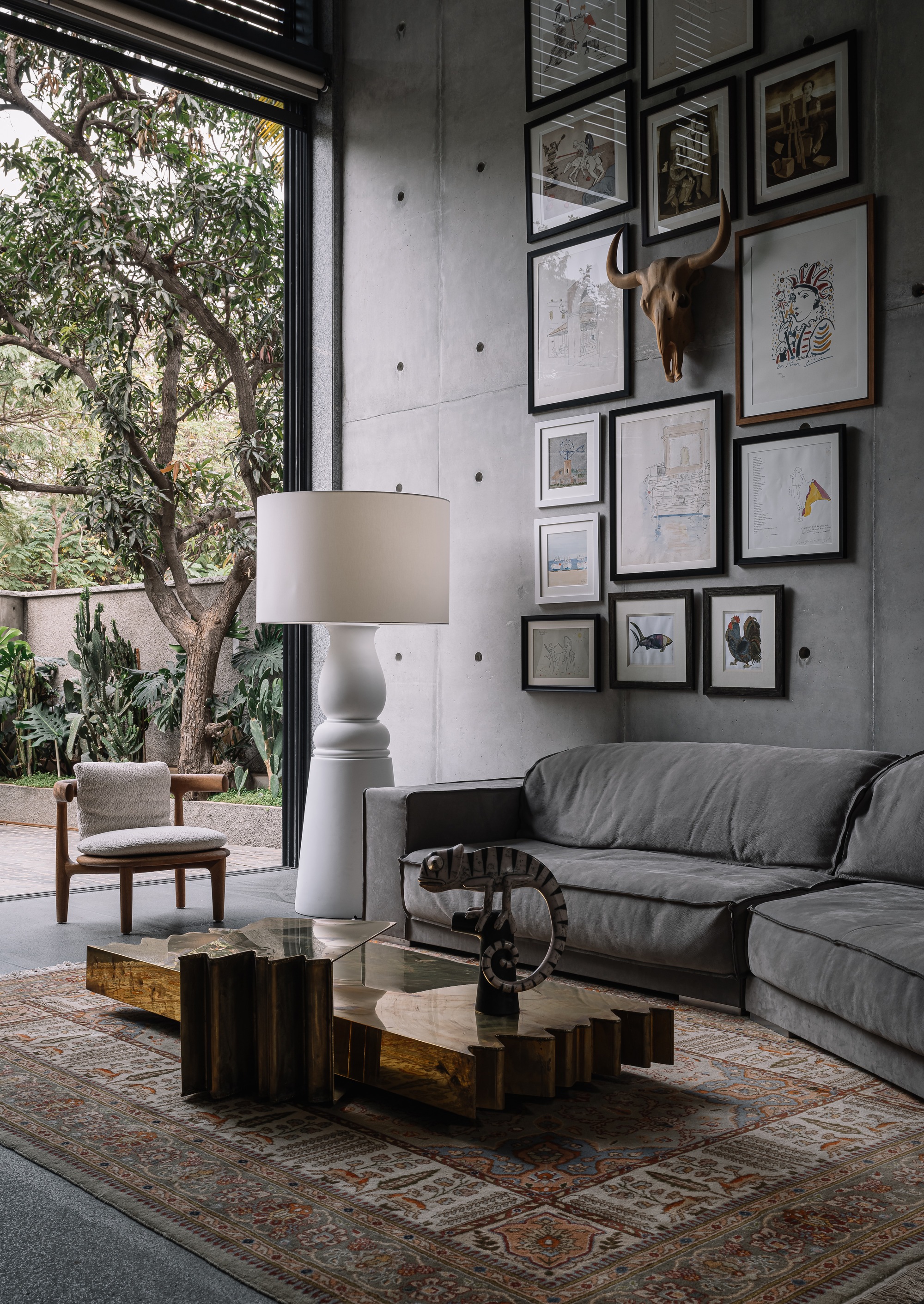 Double-height living room with concrete wall, framed art gallery, and full-height glazing opening to planted courtyard