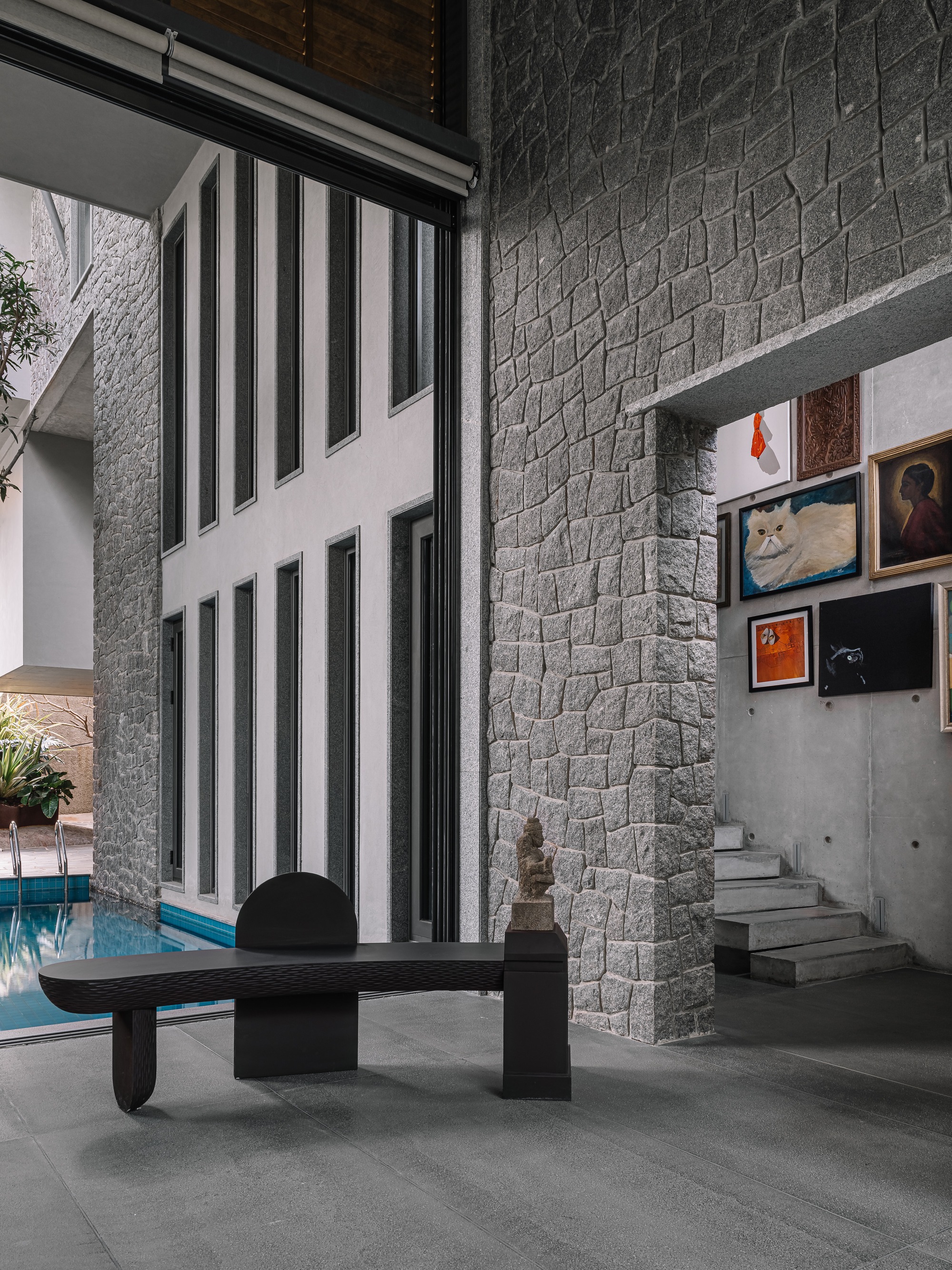 Interior courtyard with textured stone wall, concrete staircase, and floor-to-ceiling windows overlooking a pool