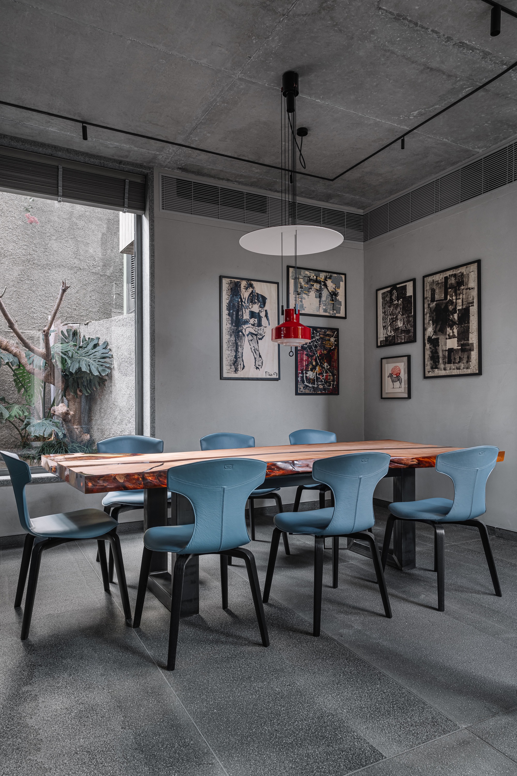 Dining room with live-edge timber table, blue upholstered chairs, and exposed concrete ceiling with pendant light