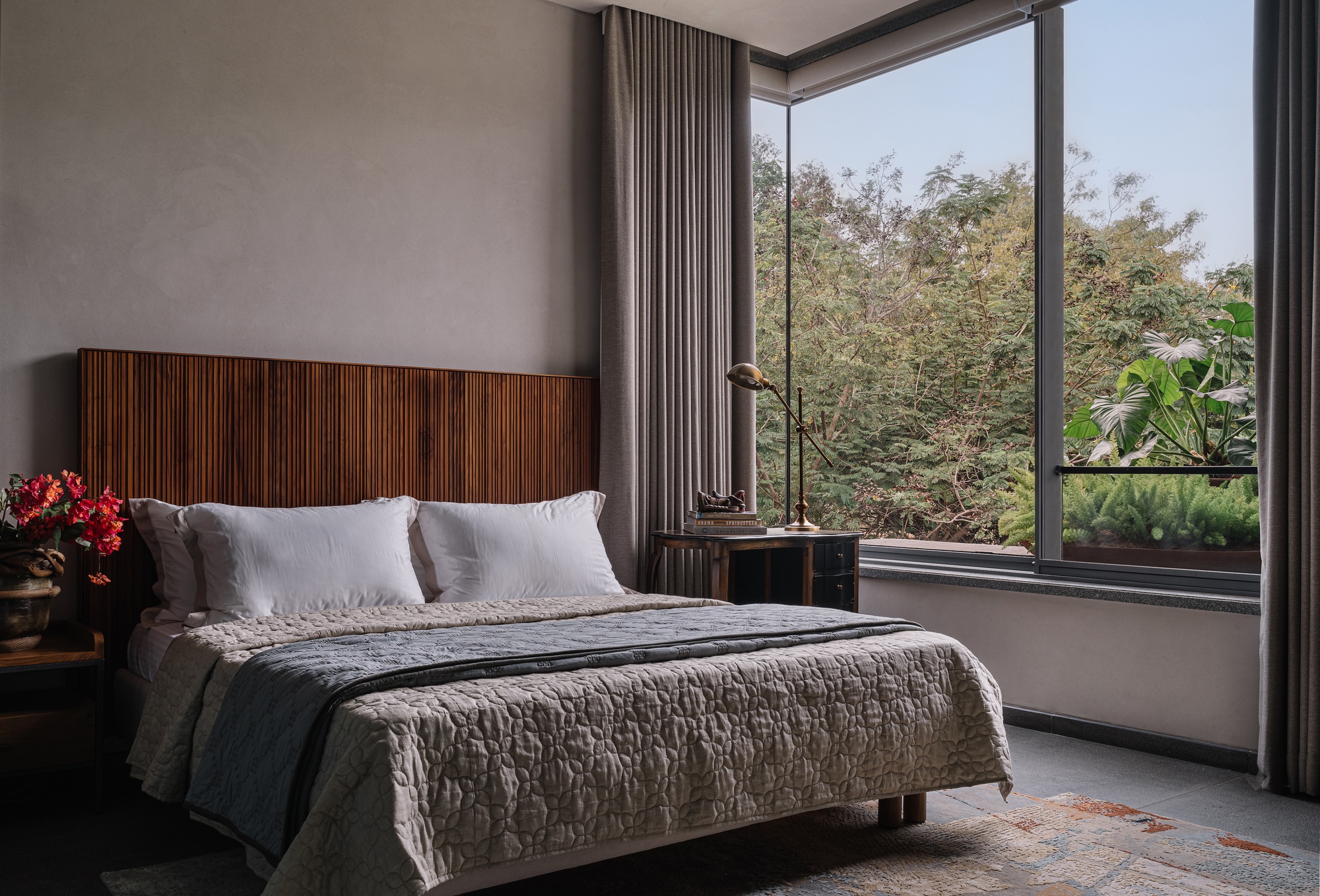 Bedroom with horizontal slat timber headboard and corner windows overlooking mature trees