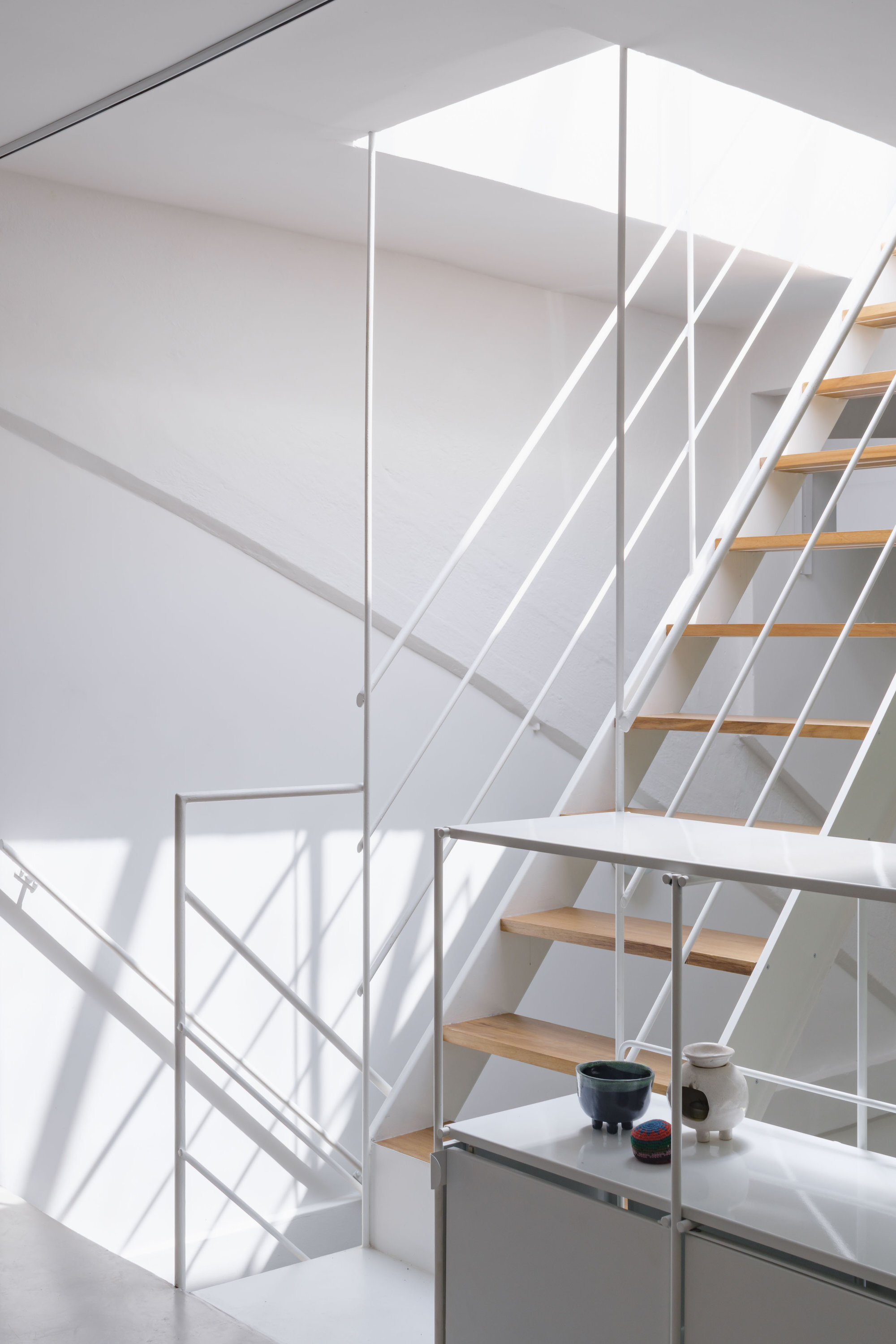 Open timber staircase with white steel railings climbing through a double-height volume in bright daylight