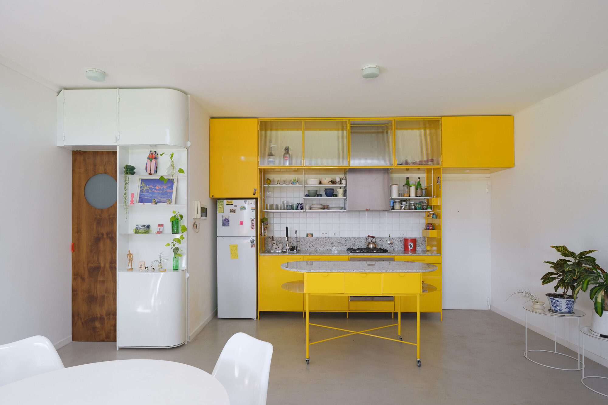 Yellow lacquered kitchen cabinetry with curved island and sliding glass doors beneath white upper units