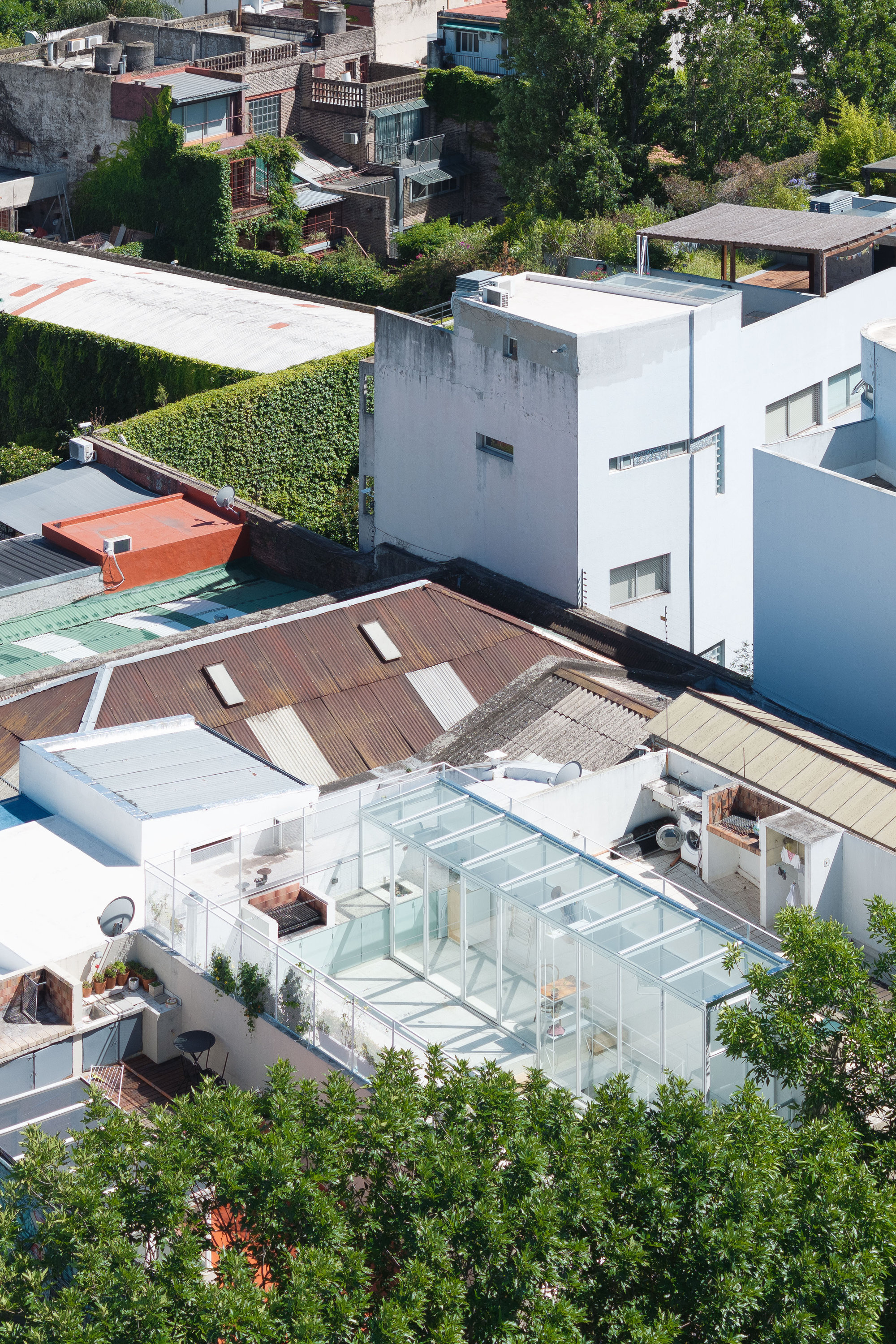 Aerial view of white rooftop terrace with glass enclosure and timber deck among neighboring houses