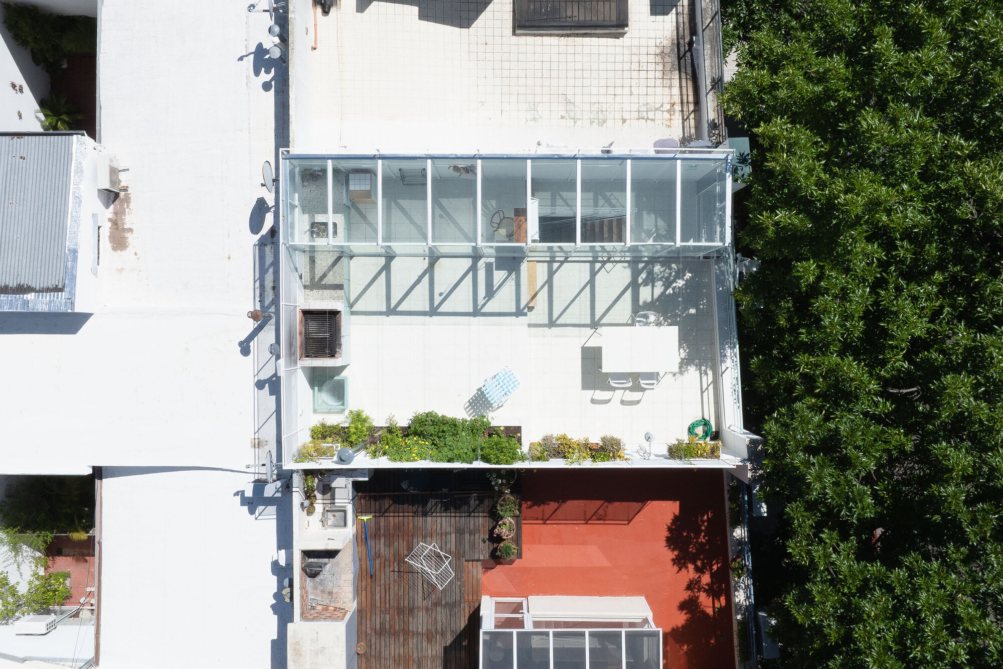 Aerial view of stacked glass volumes on a white facade with planted terrace and adjacent trees