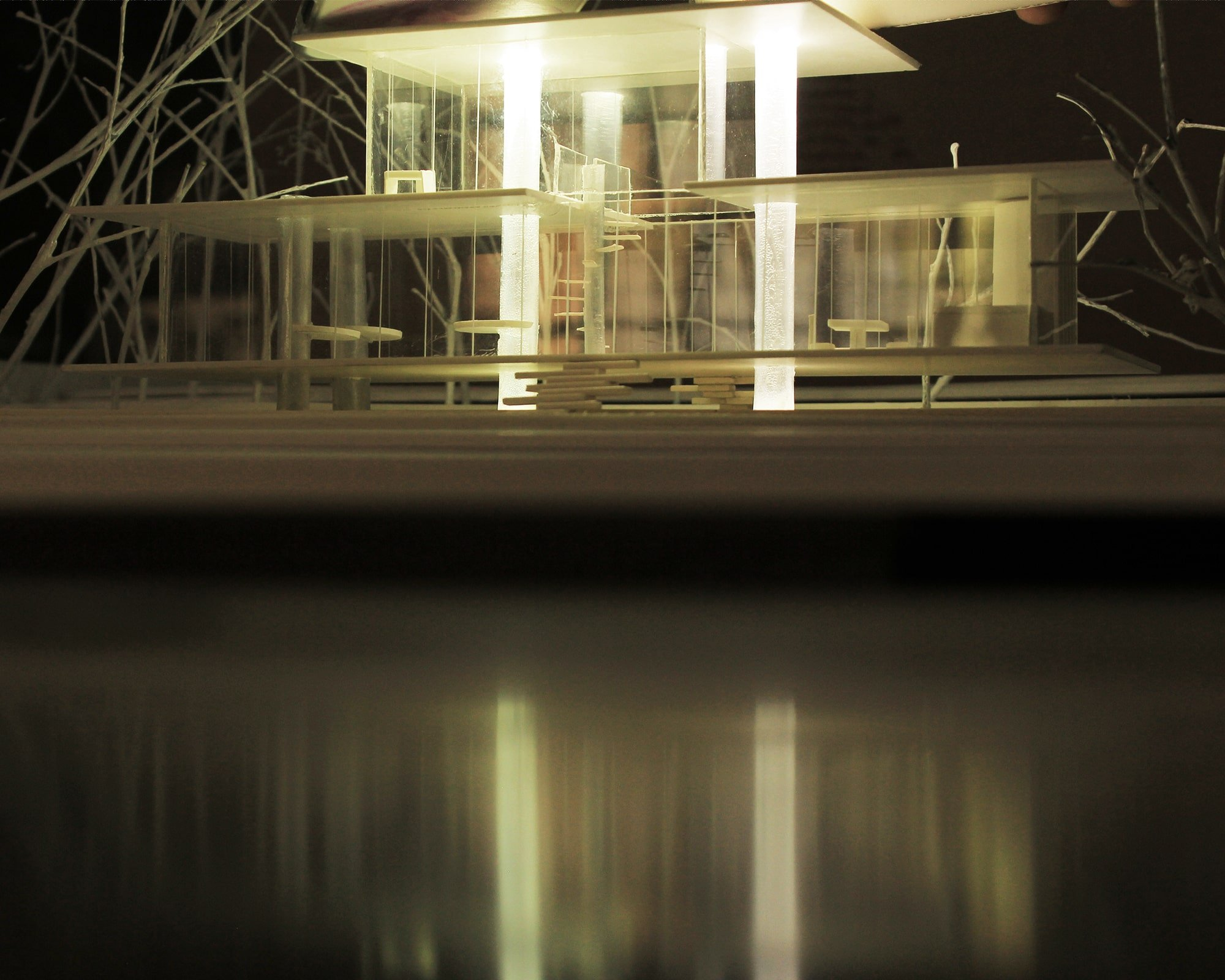 Illuminated physical model highlights layered glass volumes, horizontal planes, and slender structural elements.