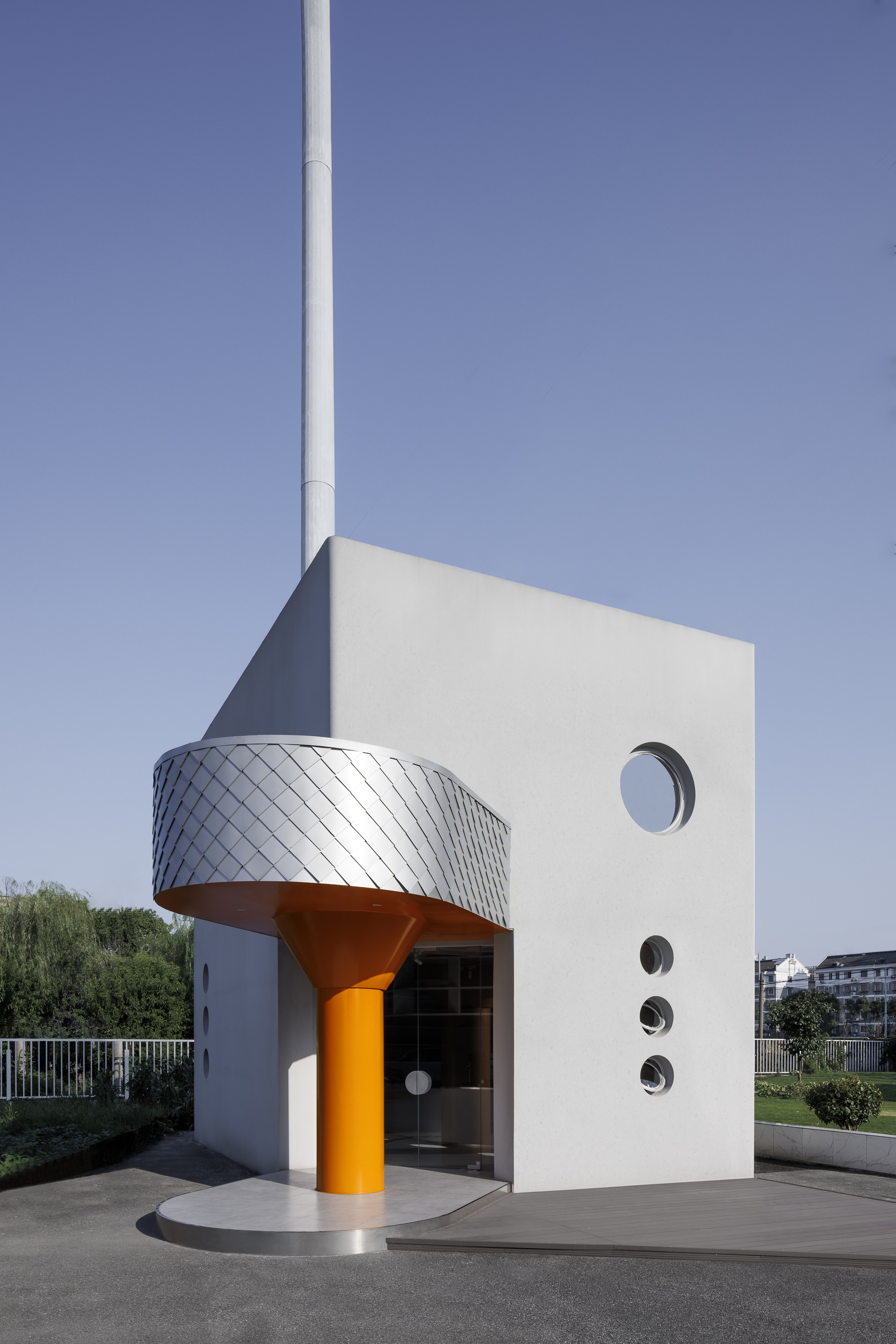 White cubic volume with orange column, silver-scaled canopy, and circular porthole windows under clear sky