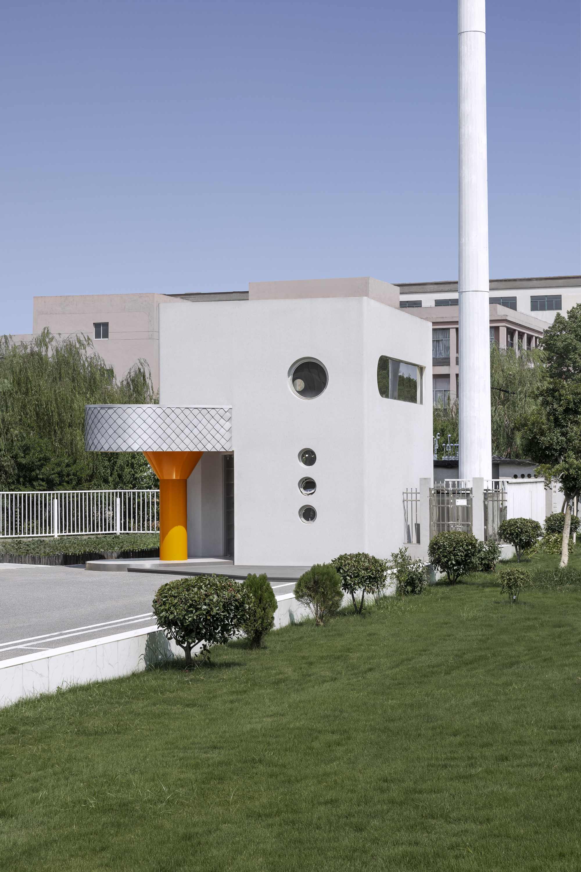 Entrance facade with scalloped metal canopy and orange column beside landscaped lawn with trimmed shrubs
