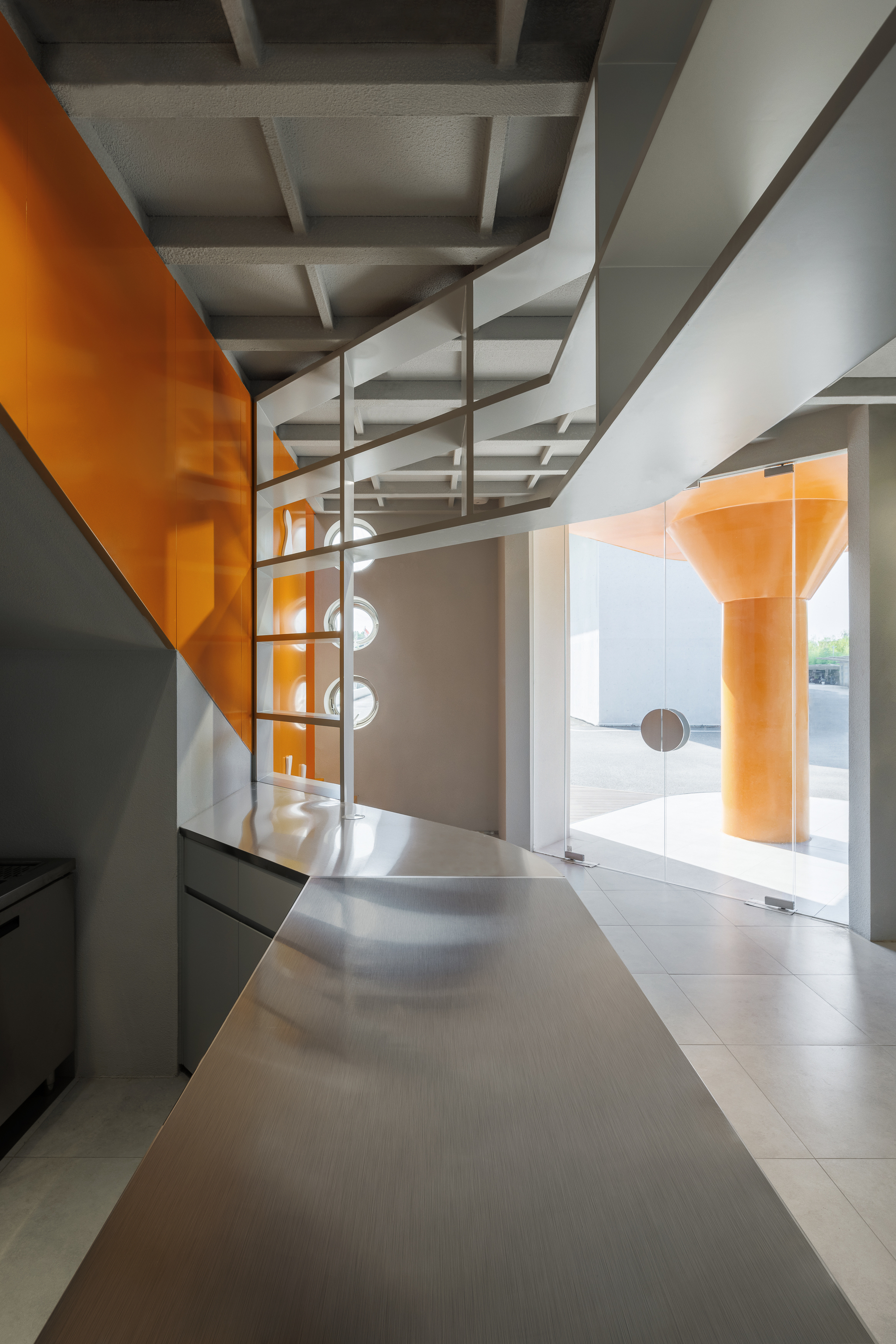 Spiral staircase beneath exposed ceiling beams with orange glass partition reflecting afternoon light