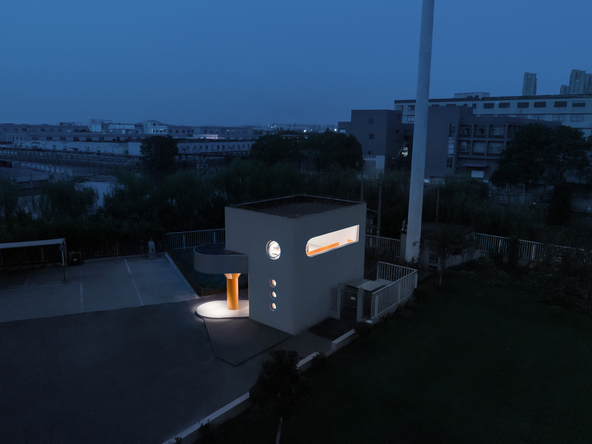 Aerial view of the illuminated white volume with glowing orange column and windows at dusk