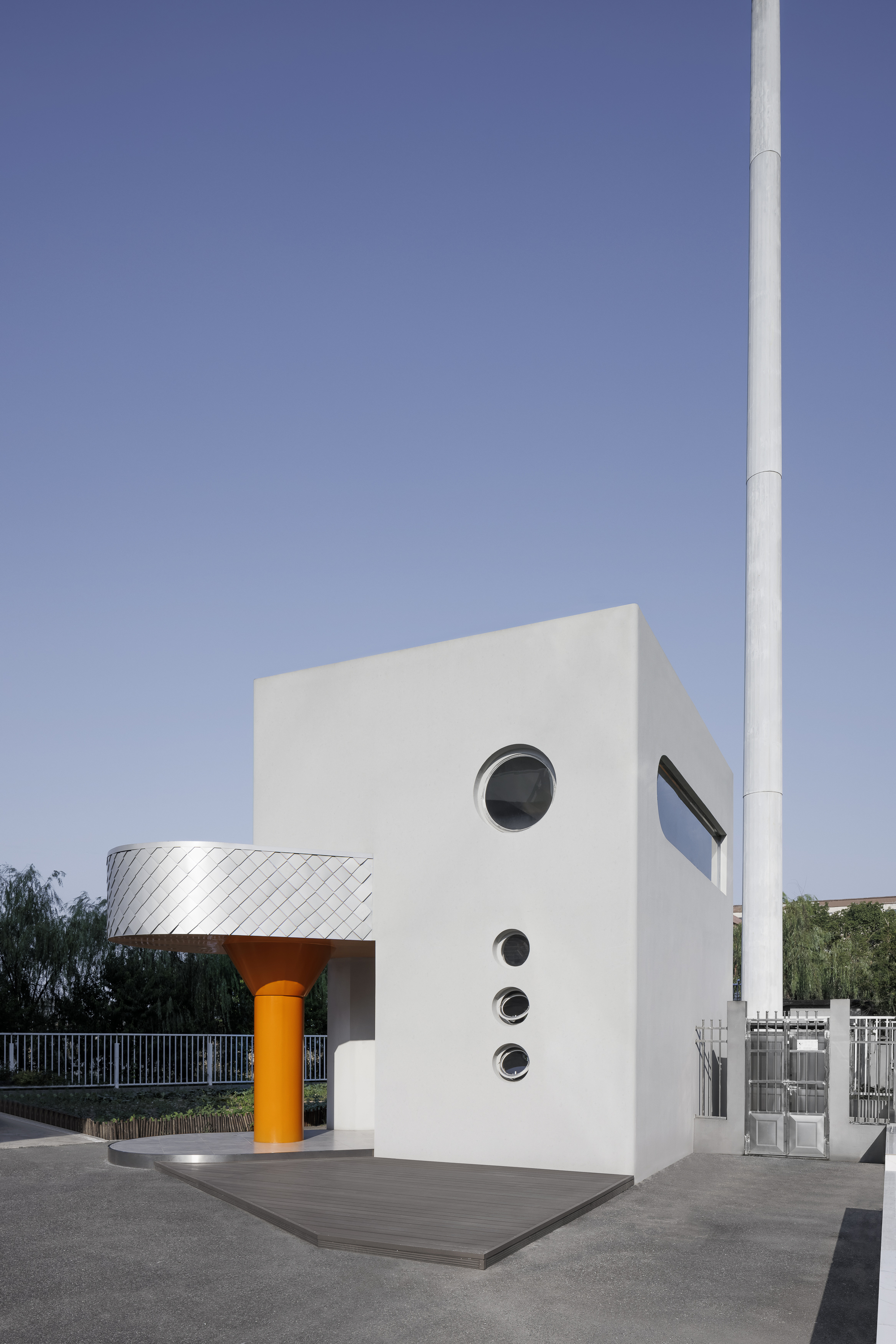 White stucco facade with stacked circular windows and angled glazing beside a white pole in daylight
