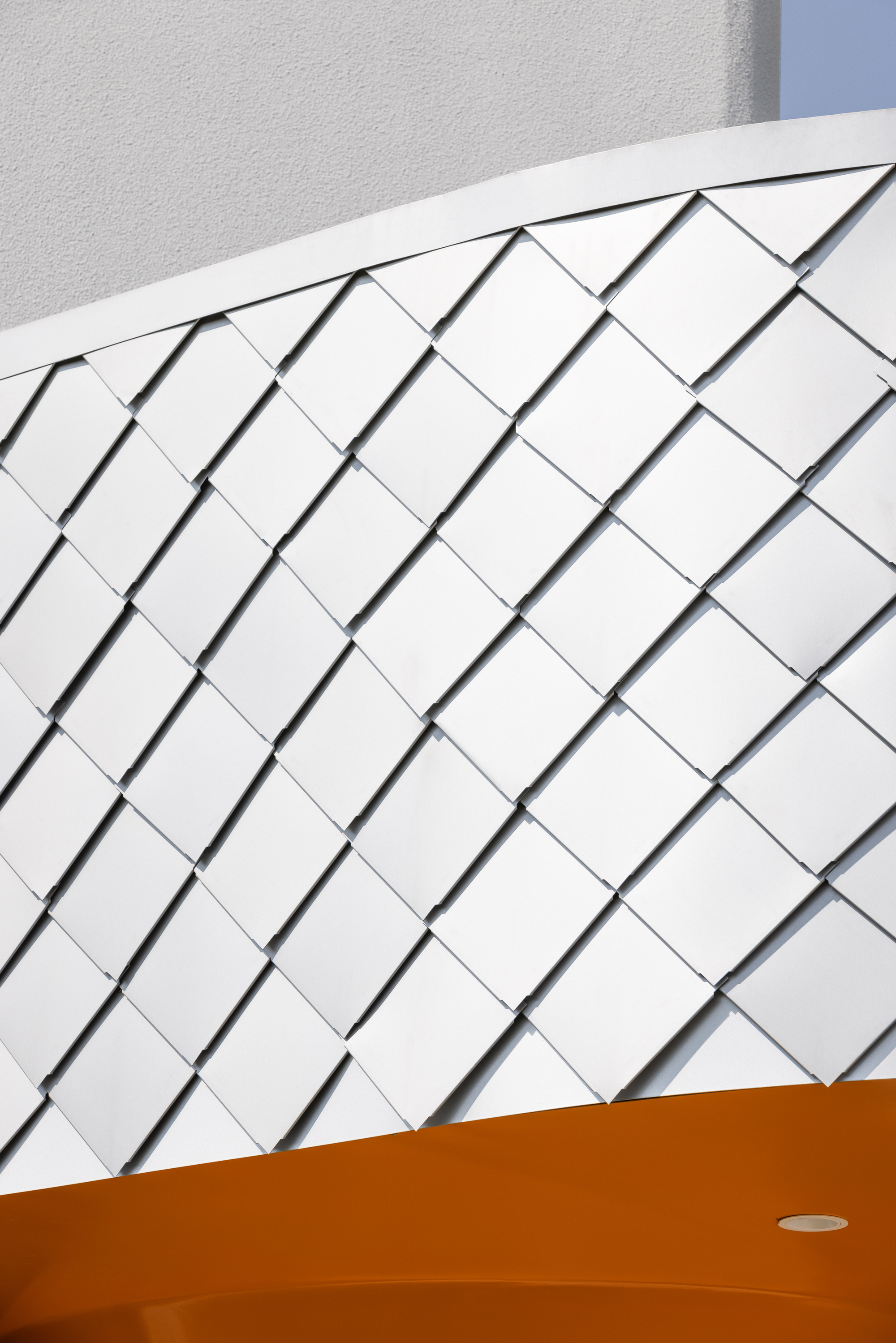 Curved white shingled wall intersecting with orange soffit under bright daylight