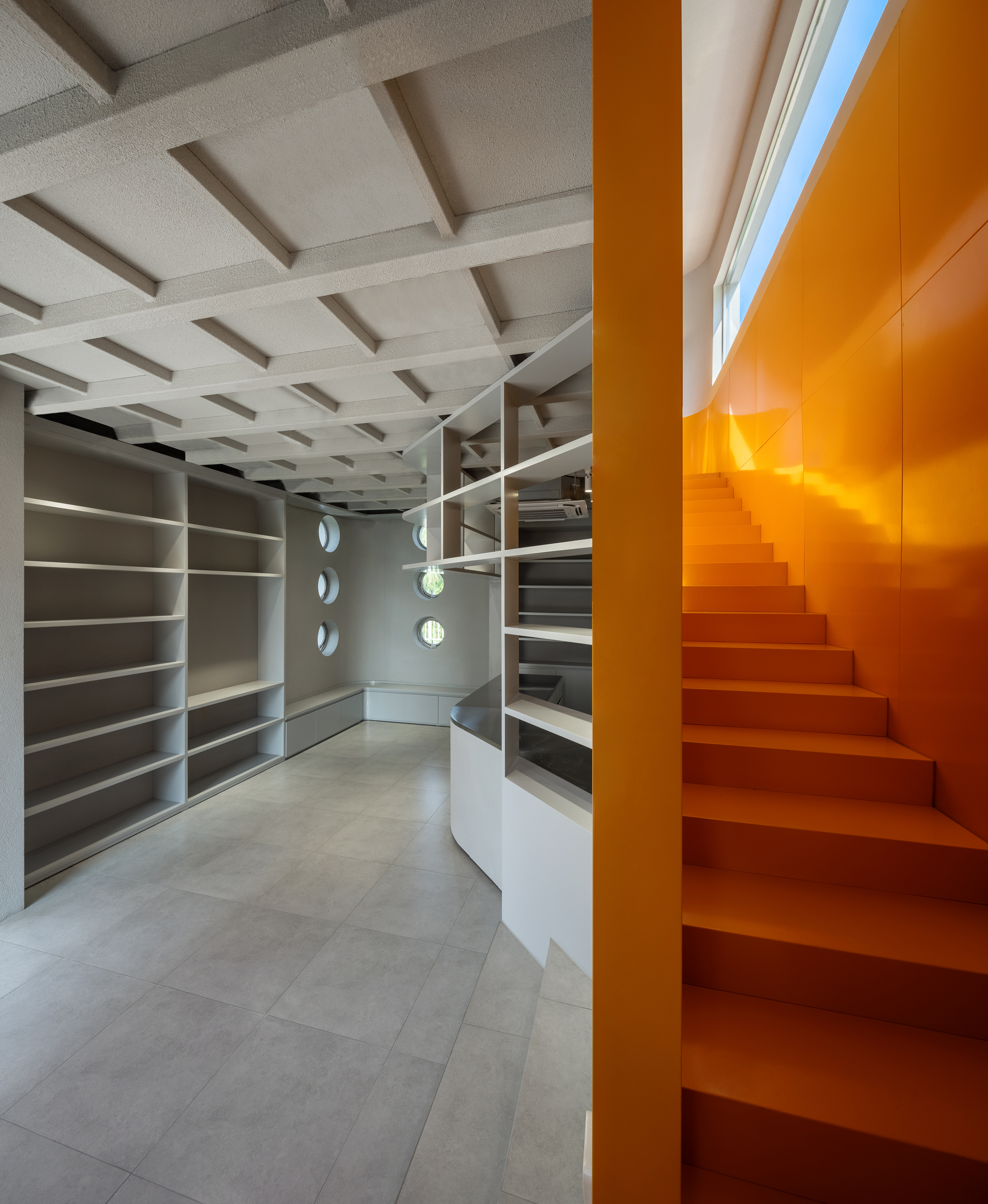 Interior library space with coffered ceiling and orange metal staircase rising beside white shelving