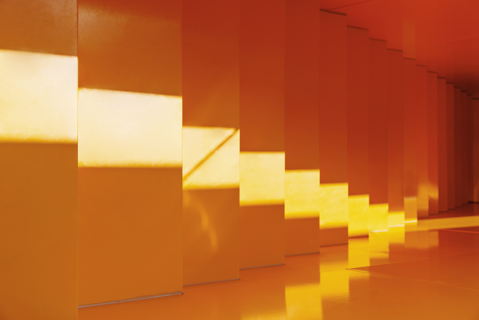 Orange staircase illuminated by angular sunlight streaming through narrow openings in the wall