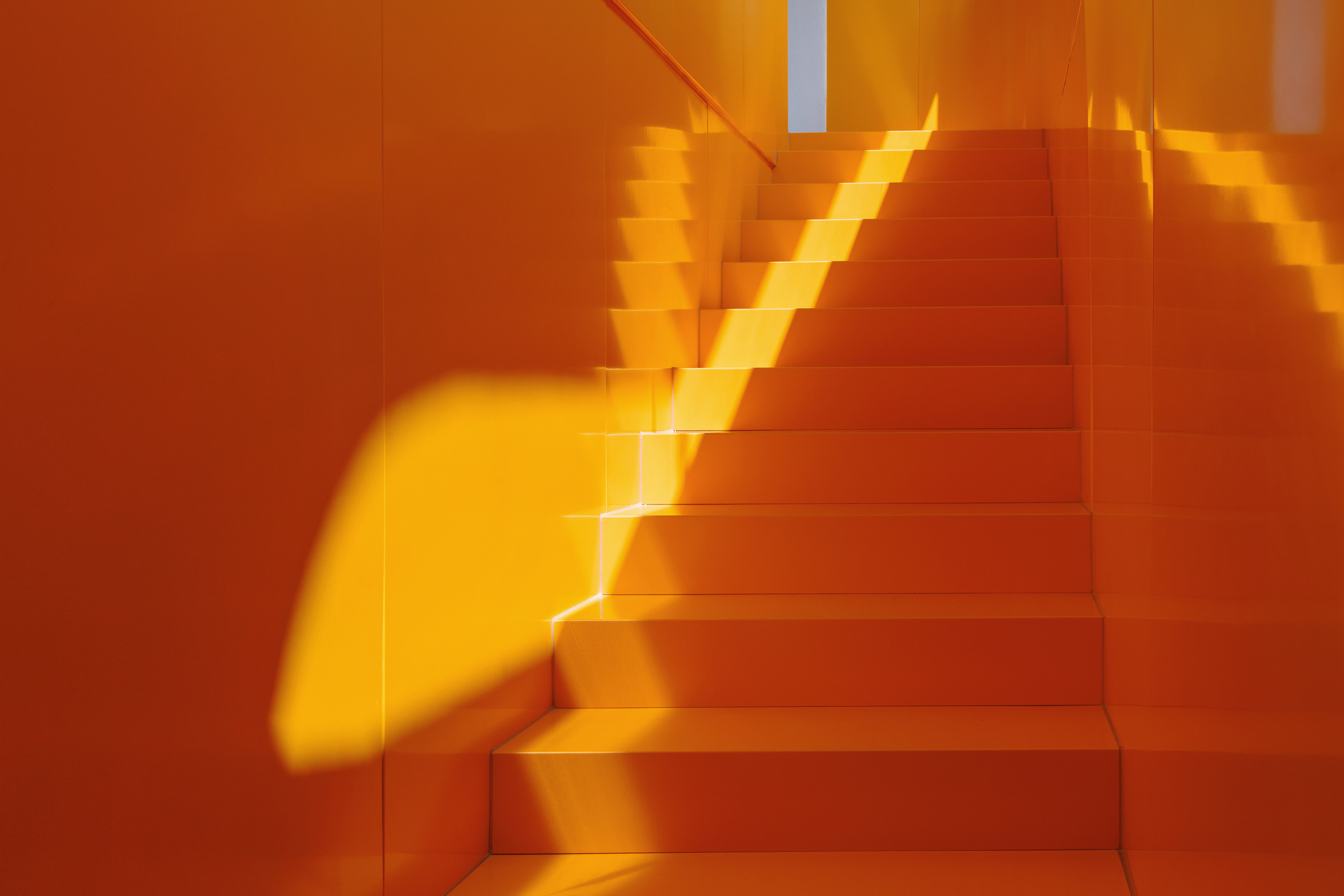Orange staircase with dramatic shadows cast by skylight opening above