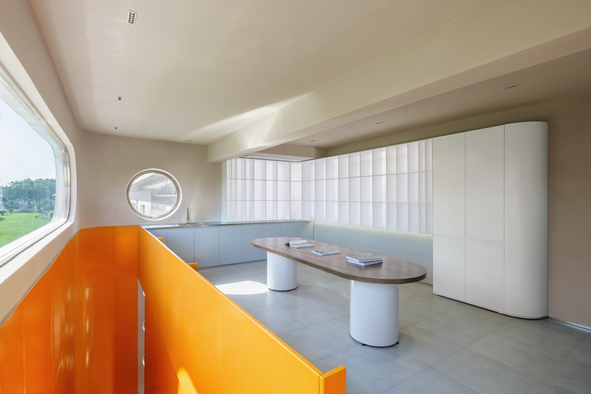 Interior space with orange bench seating, oval table, and white quilted wall panels beneath a circular window