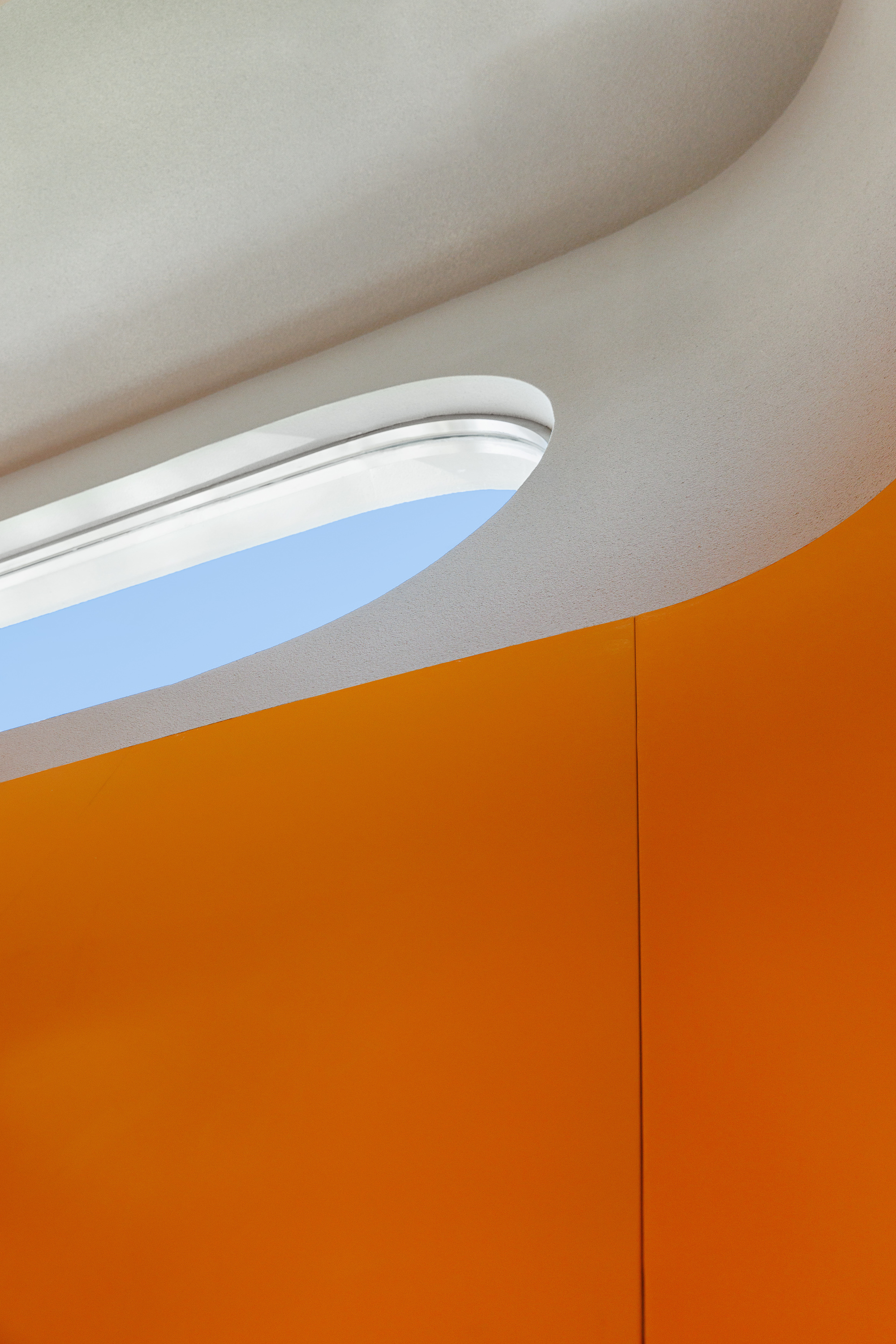 Detail of oval skylight meeting orange wall panels against a curved white ceiling