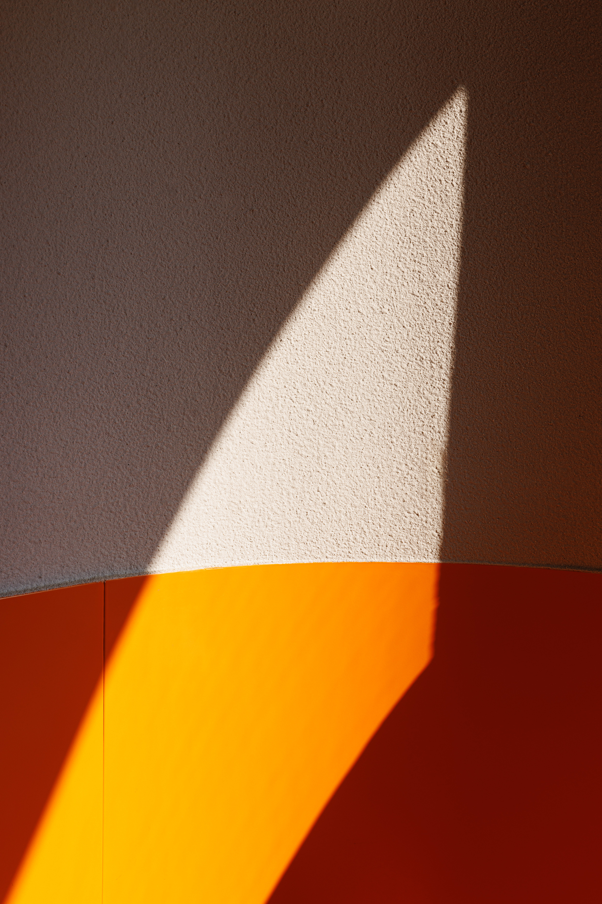 Triangular shadow cast across textured wall above orange curved cabinetry in afternoon light