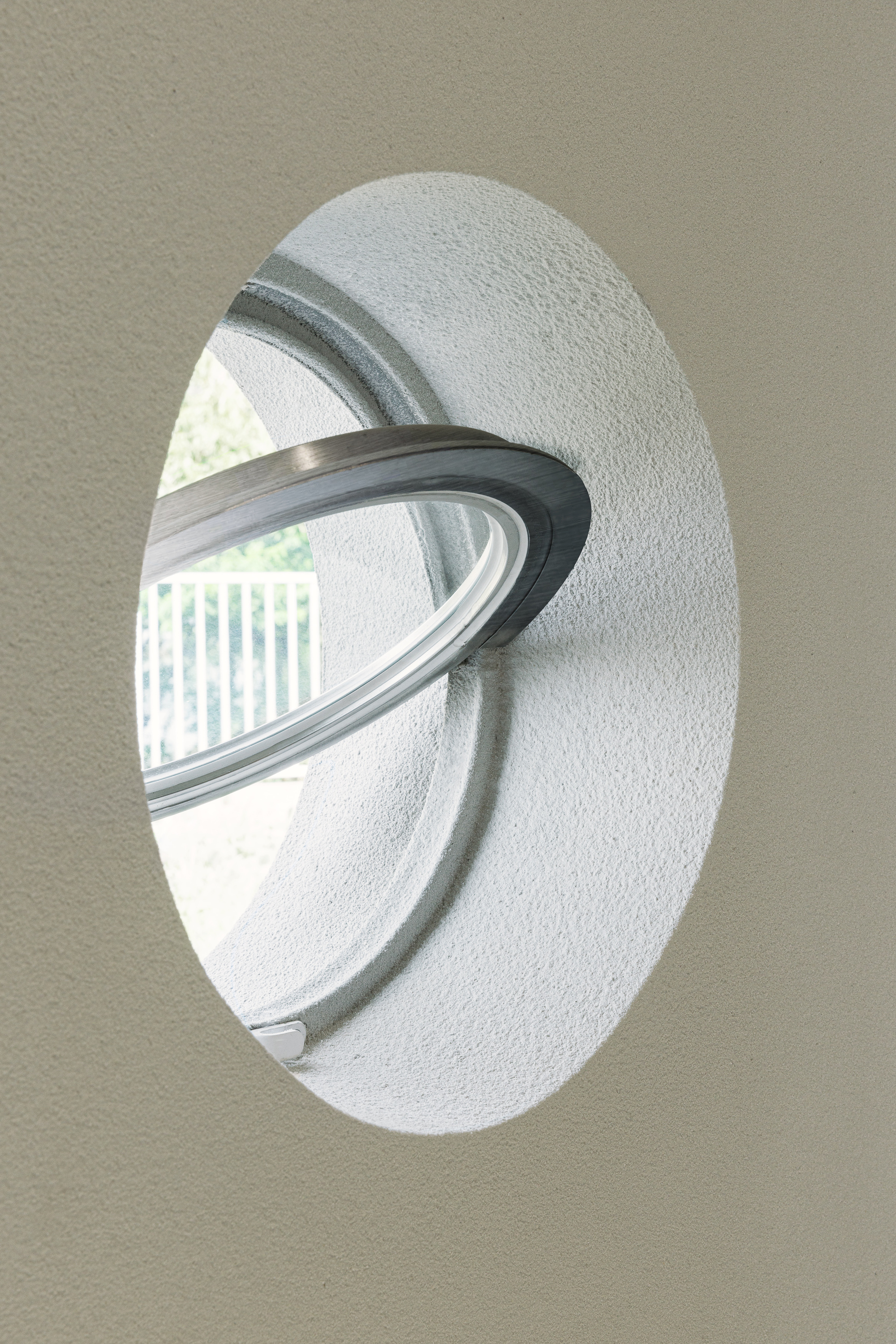 Circular window with stainless steel reveal set into textured white wall