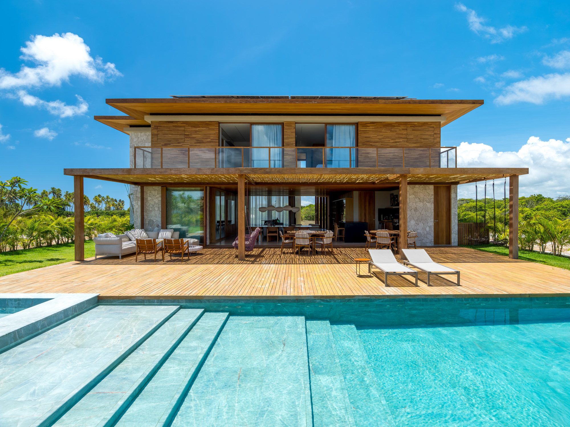 Rear facade with timber cladding and expansive decking overlooking the swimming pool on a sunny day