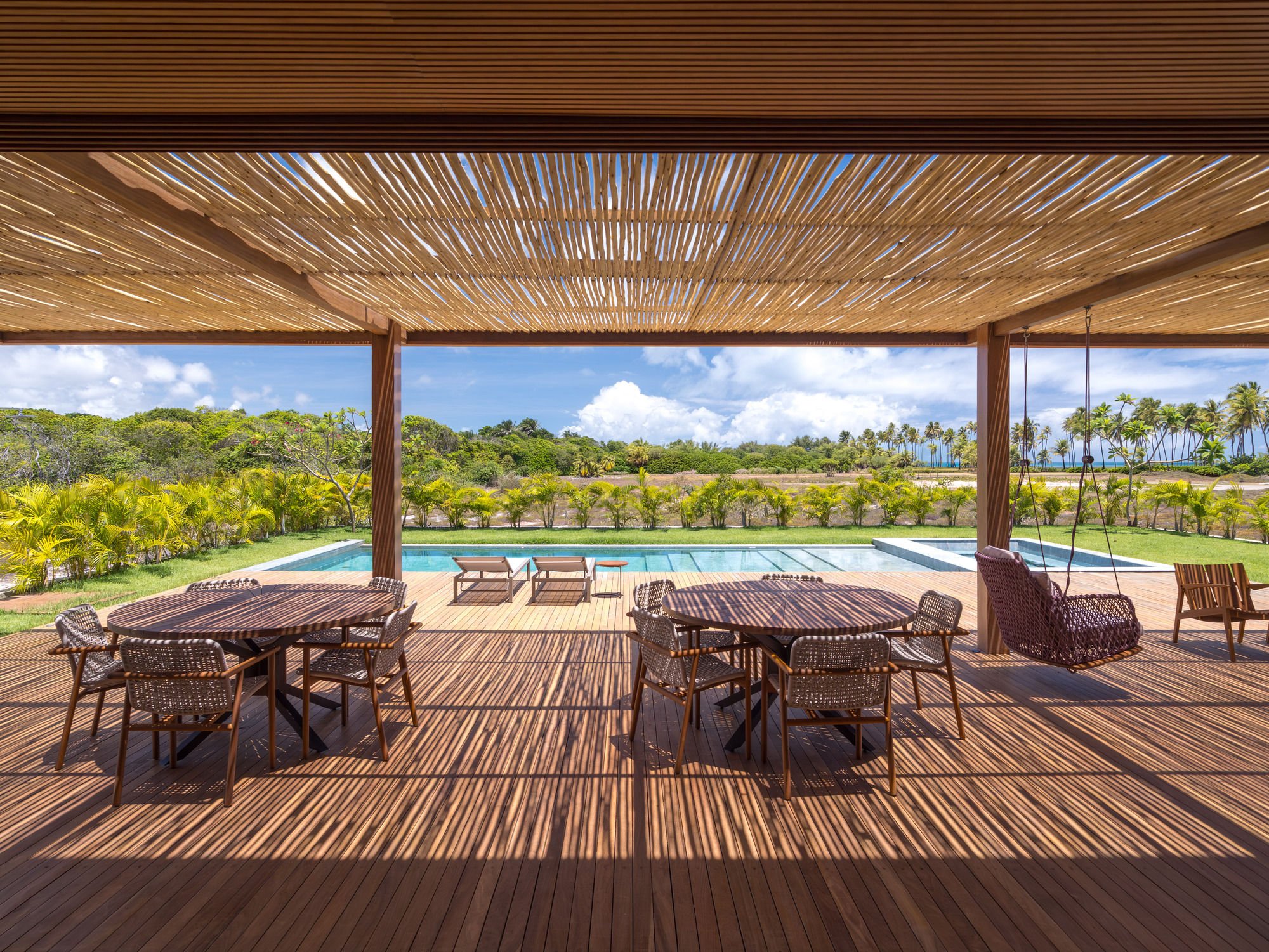Covered terrace with slatted timber ceiling and wicker furniture facing the pool and lawn beyond