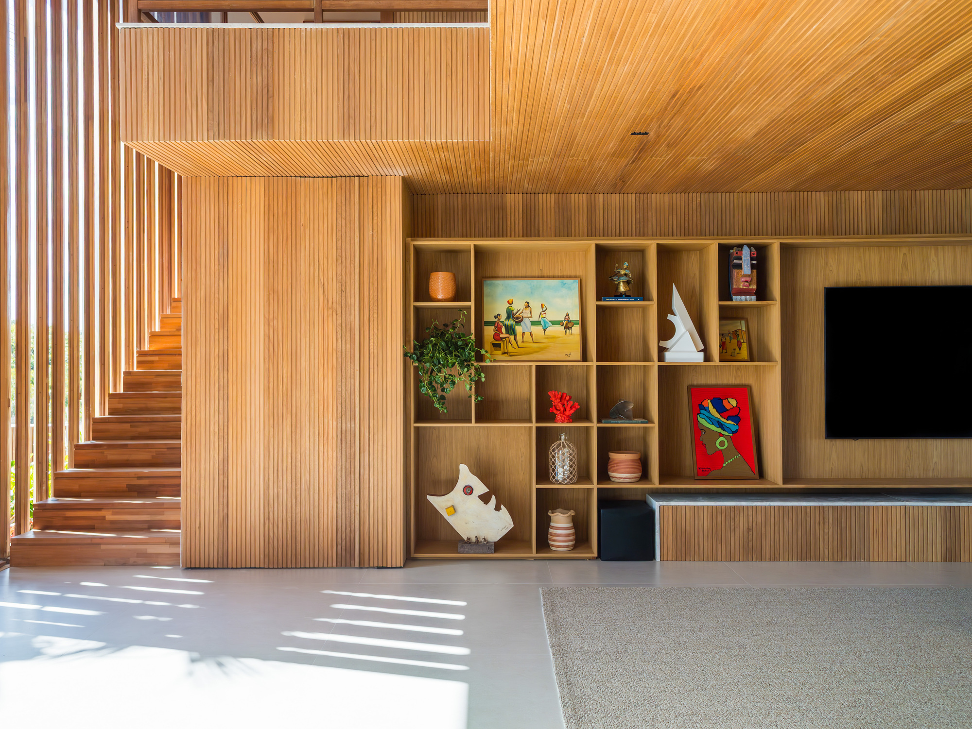 Timber-clad staircase beside the media wall with sunlight patterns cast across the terrazzo floor