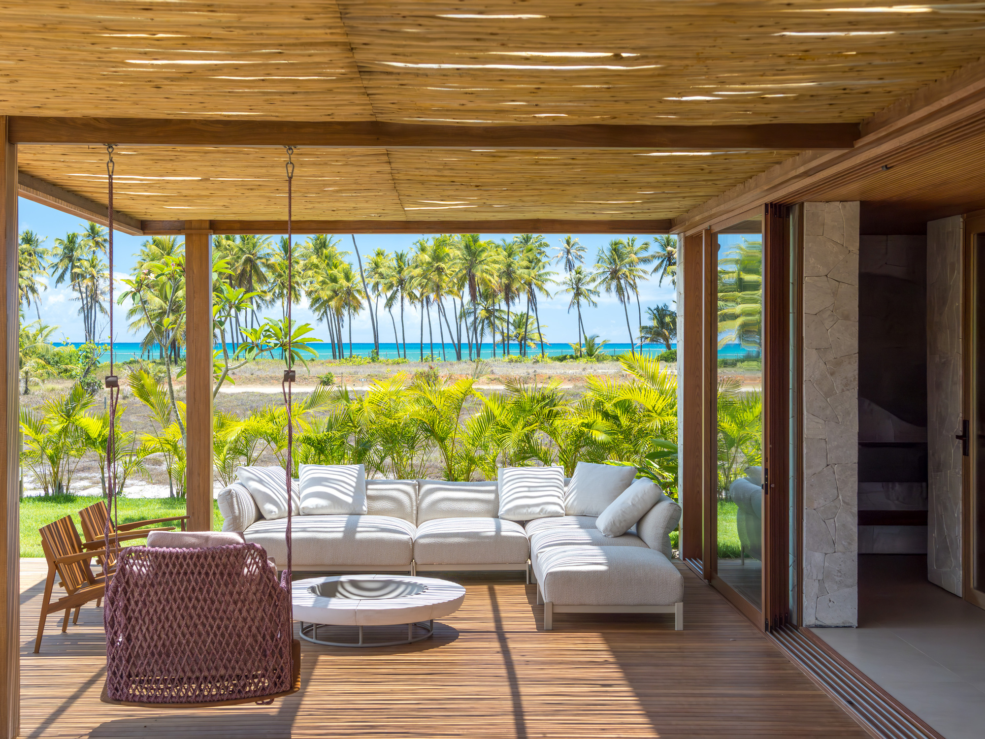 Covered terrace with slatted ceiling framing views of palm trees and coastline through open corners