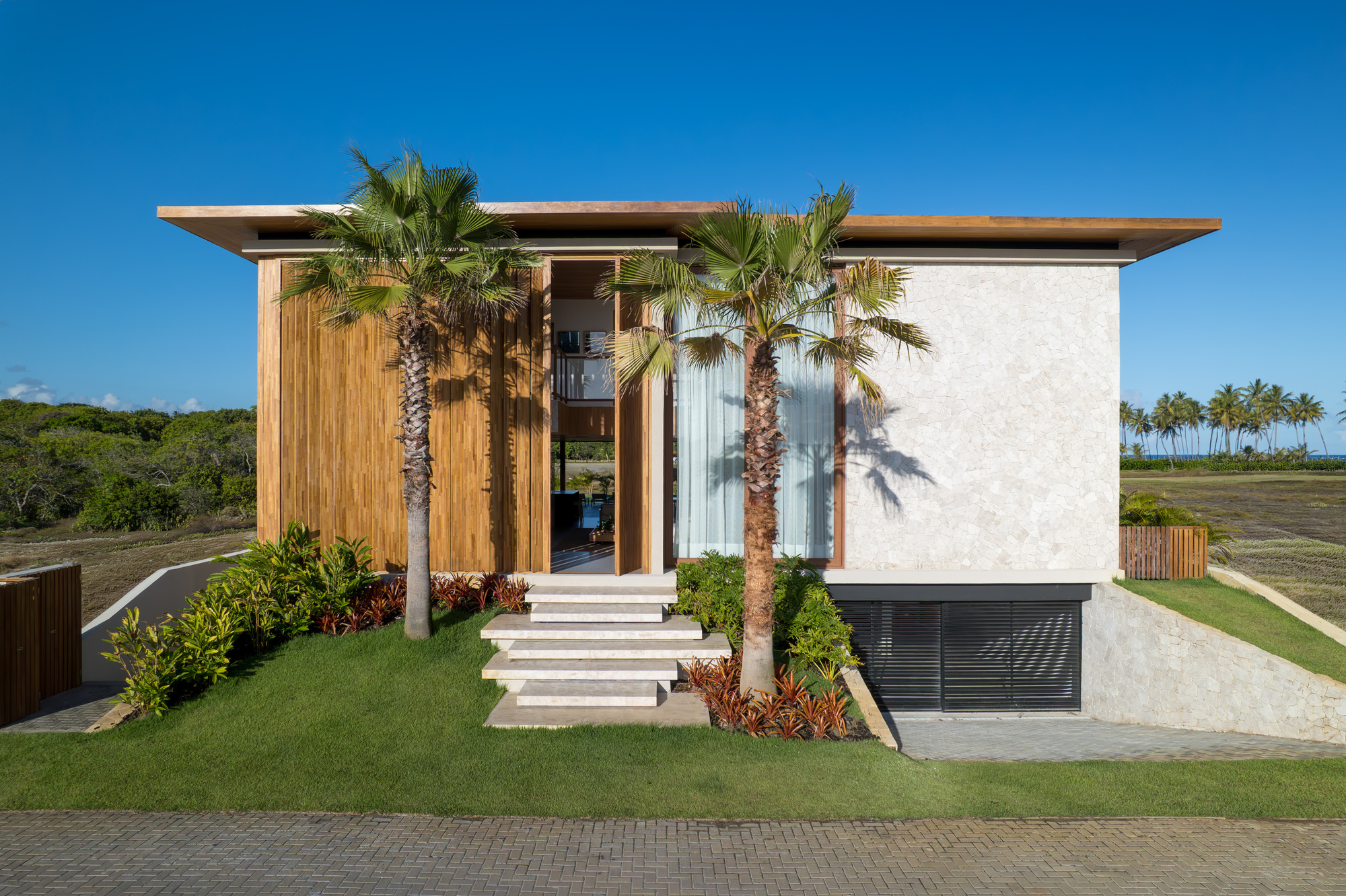 Front facade with vertical timber slats and white stucco flanked by palm trees under a clear blue sky
