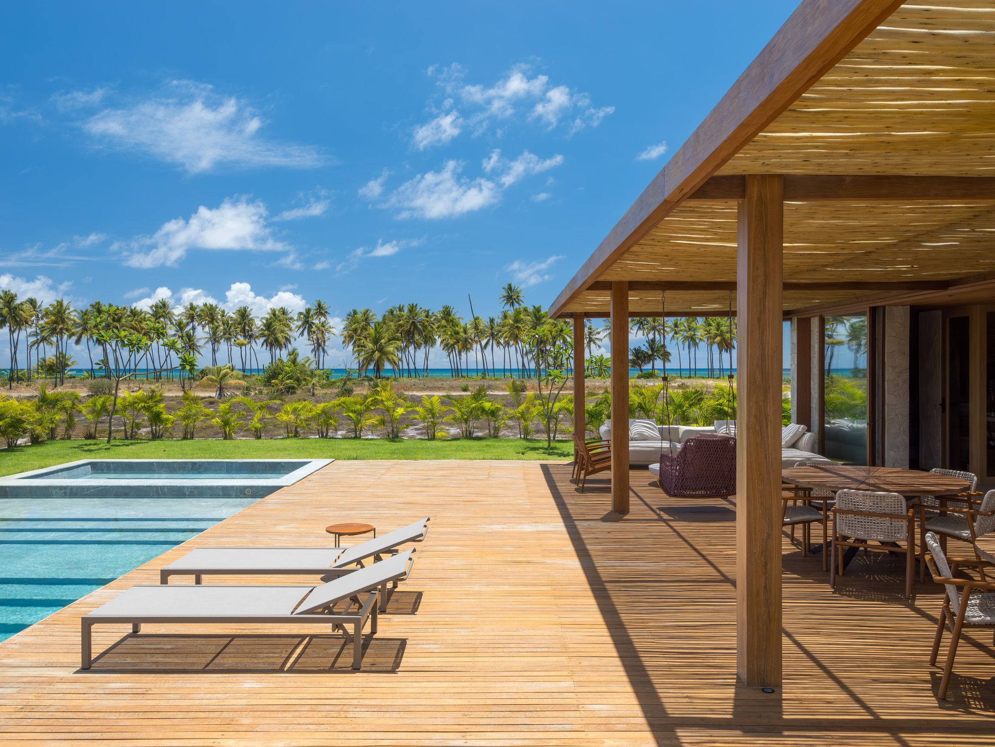Timber deck terrace with lounge chairs beside a swimming pool overlooking palm groves and ocean horizon