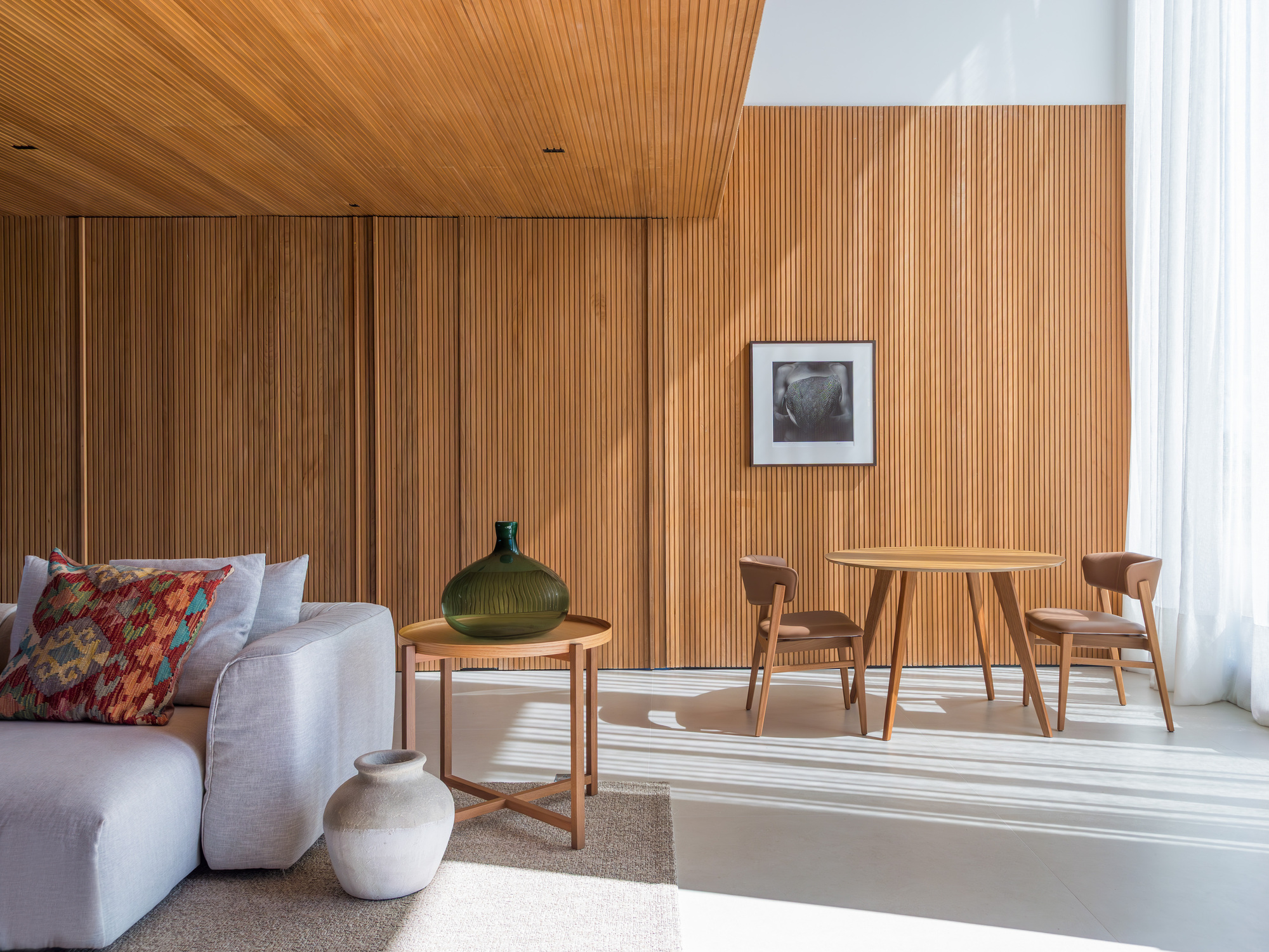 Living room corner with vertical timber-clad wall and sunlight striping across the polished concrete floor