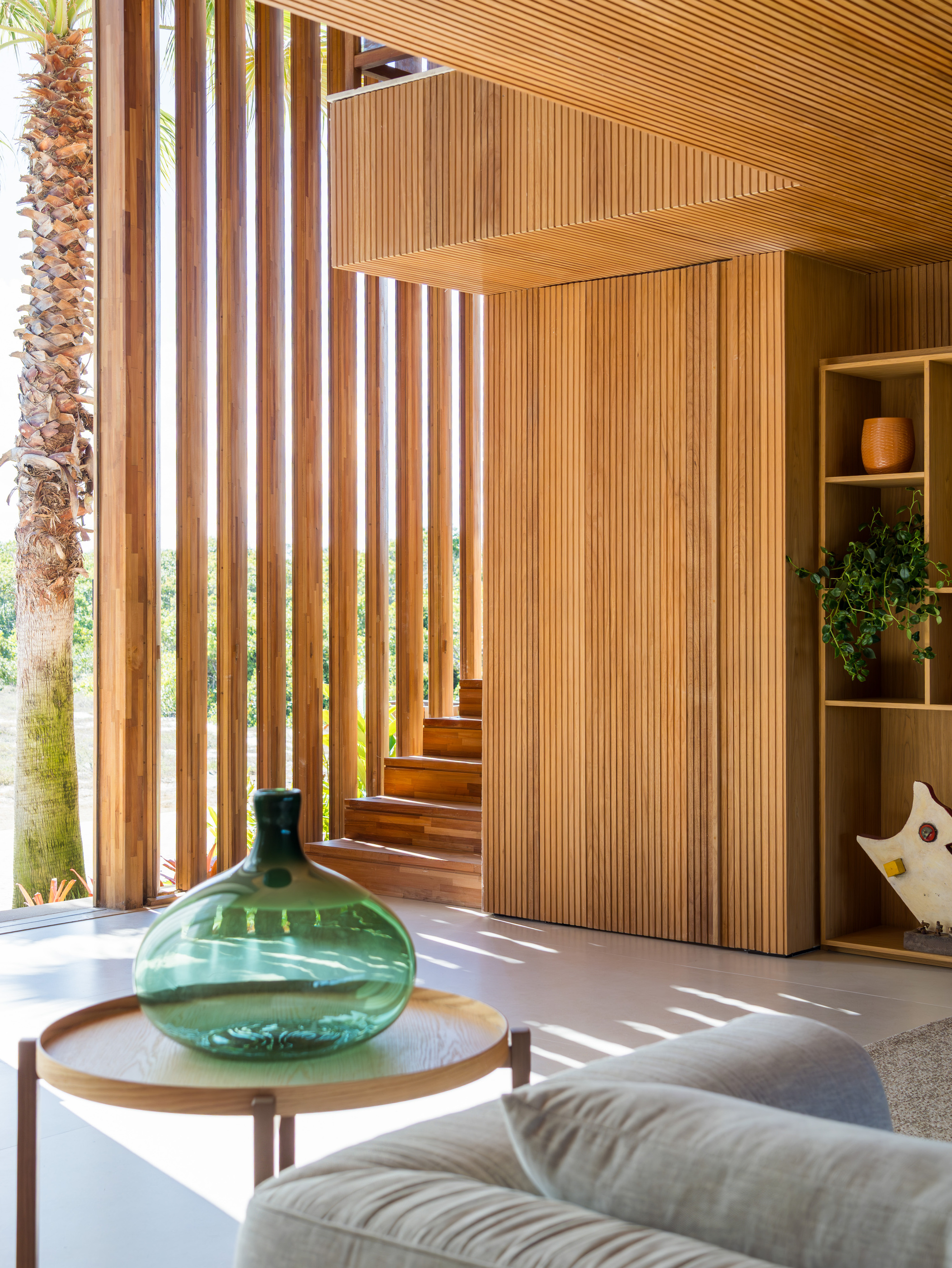Timber-clad staircase flanked by vertical wood slats with sunlight filtering through to the floor