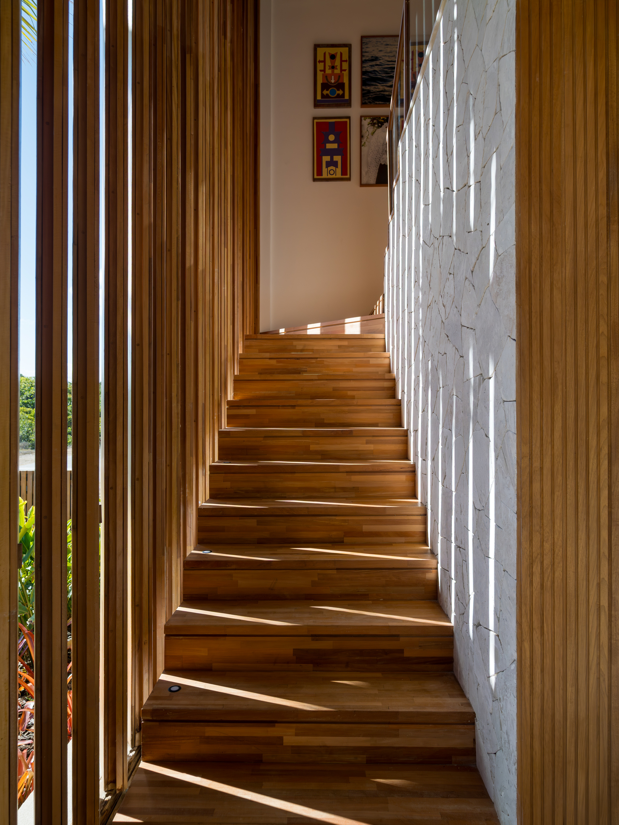 Ascending timber staircase with vertical wood screen on one side and white stone wall opposite