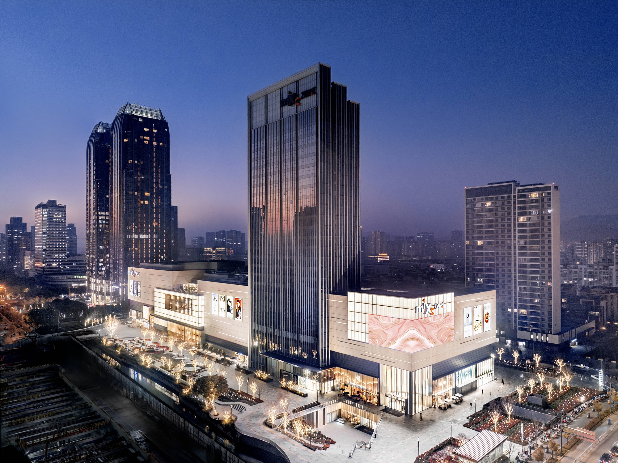 Evening view of the mixed-use complex with vertical tower and illuminated retail podium