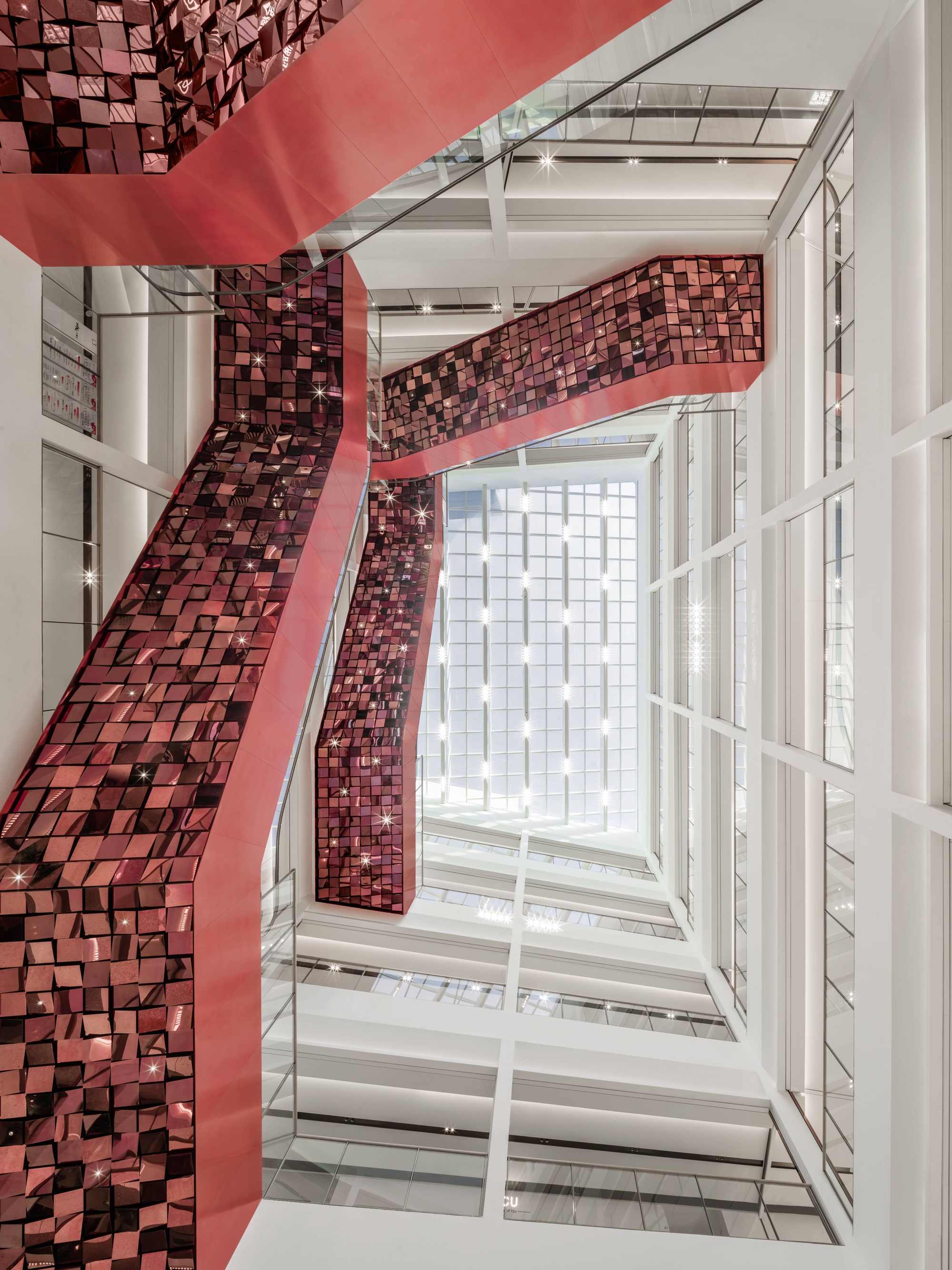 View up through the atrium void showing metallic tile-clad balconies and white structural frame