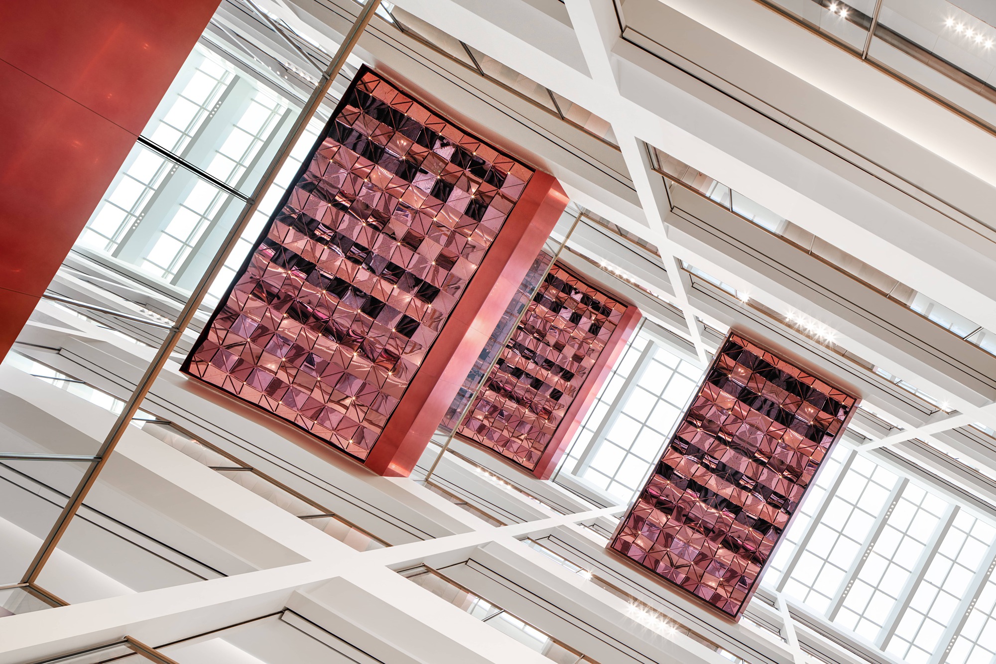 Oblique view of three metallic red tile panels suspended below white structural beams and skylight