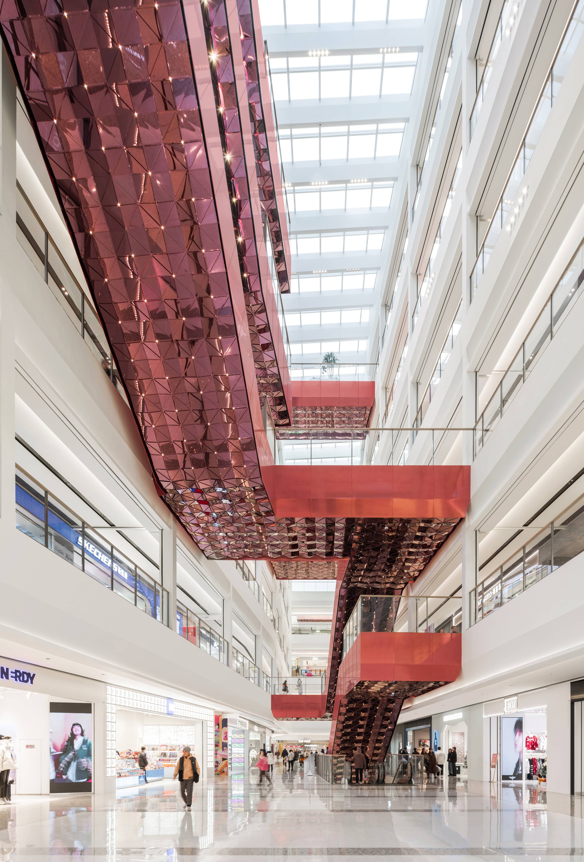 Corridor view with suspended metallic tile panels overhead and retail storefronts flanking polished floor