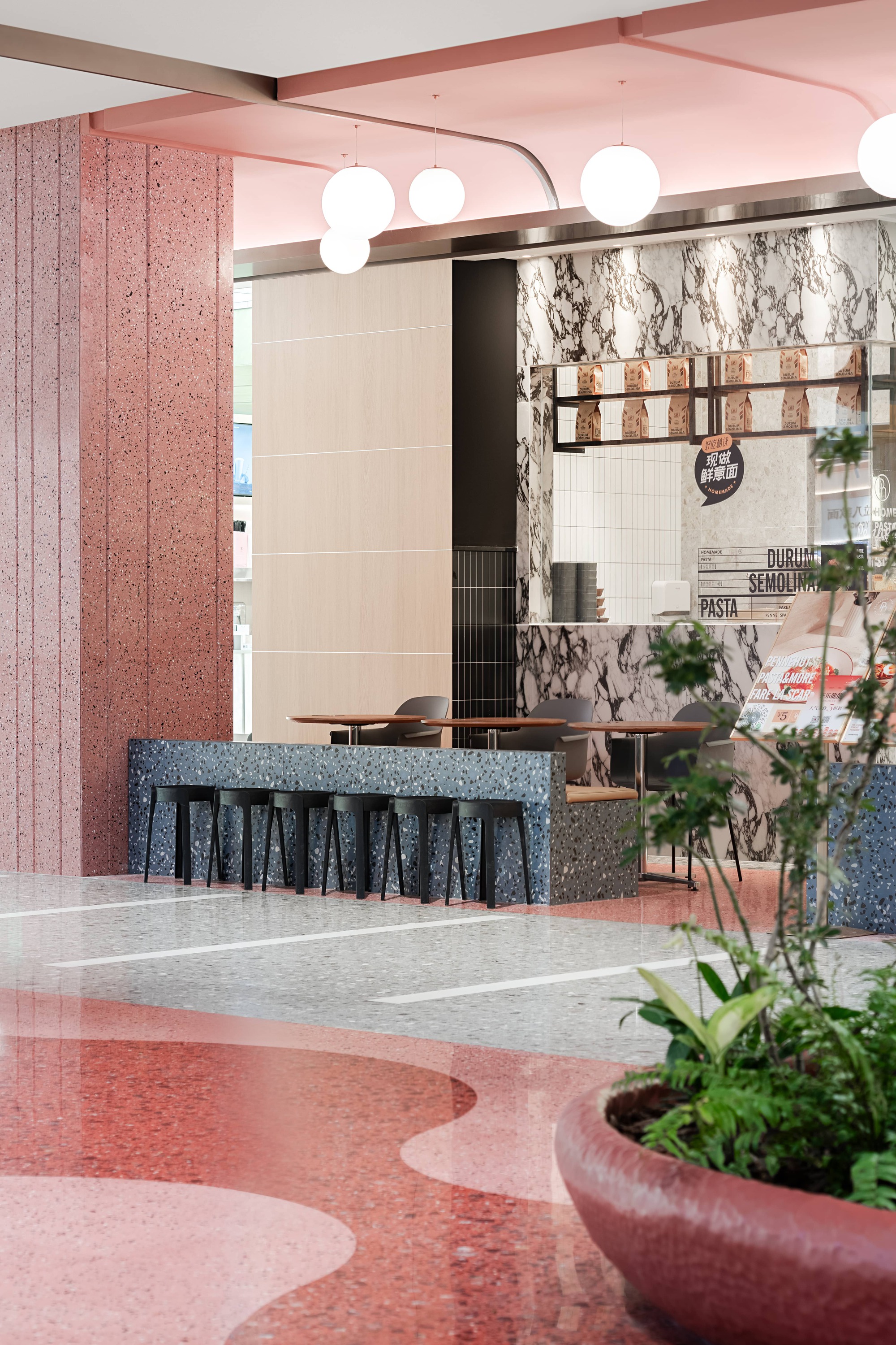 Food counter with marbled backsplash, pink terrazzo panels, blue aggregate bar, and globe pendant lights