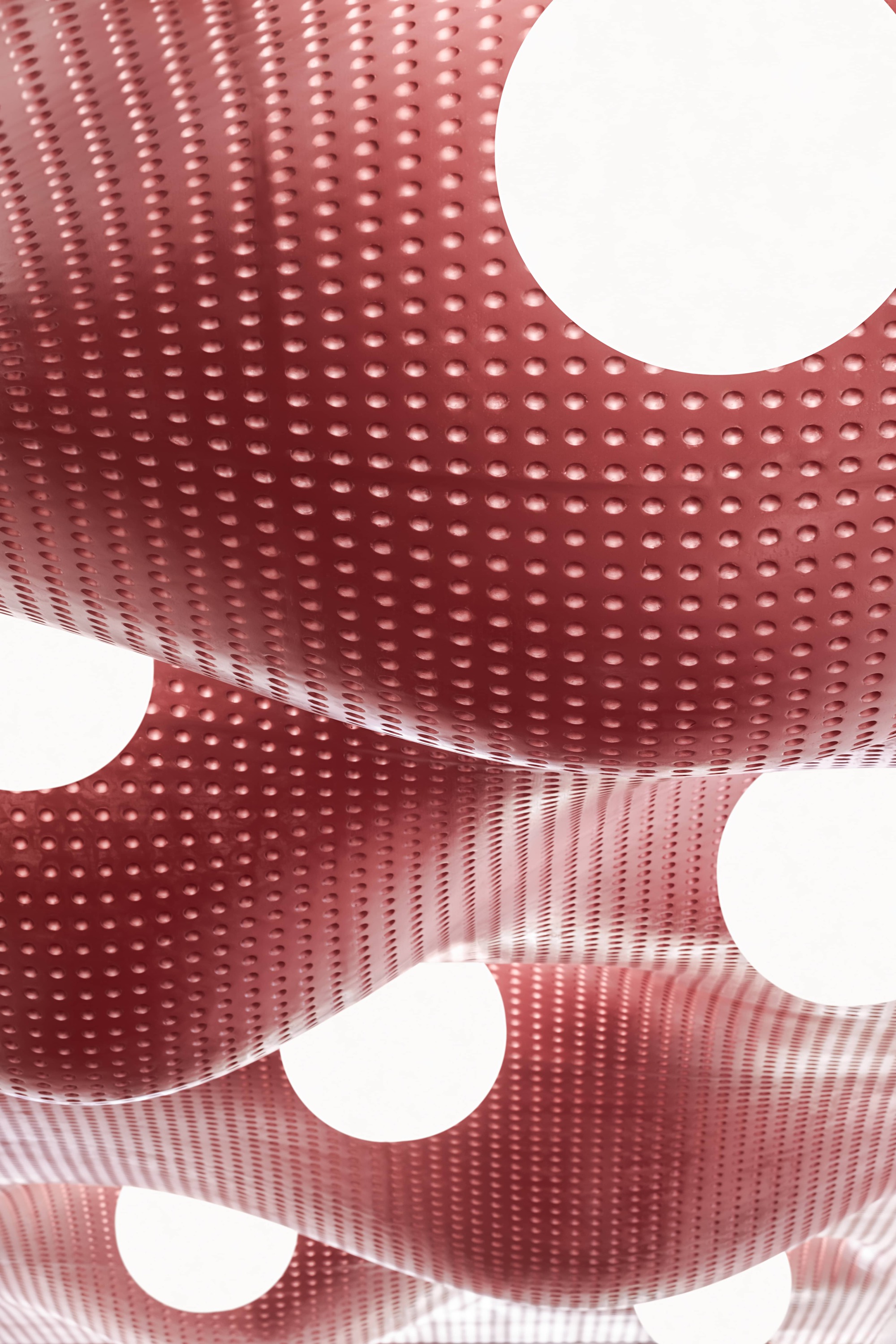 Close-up of perforated red metal ceiling panel curving around circular light openings