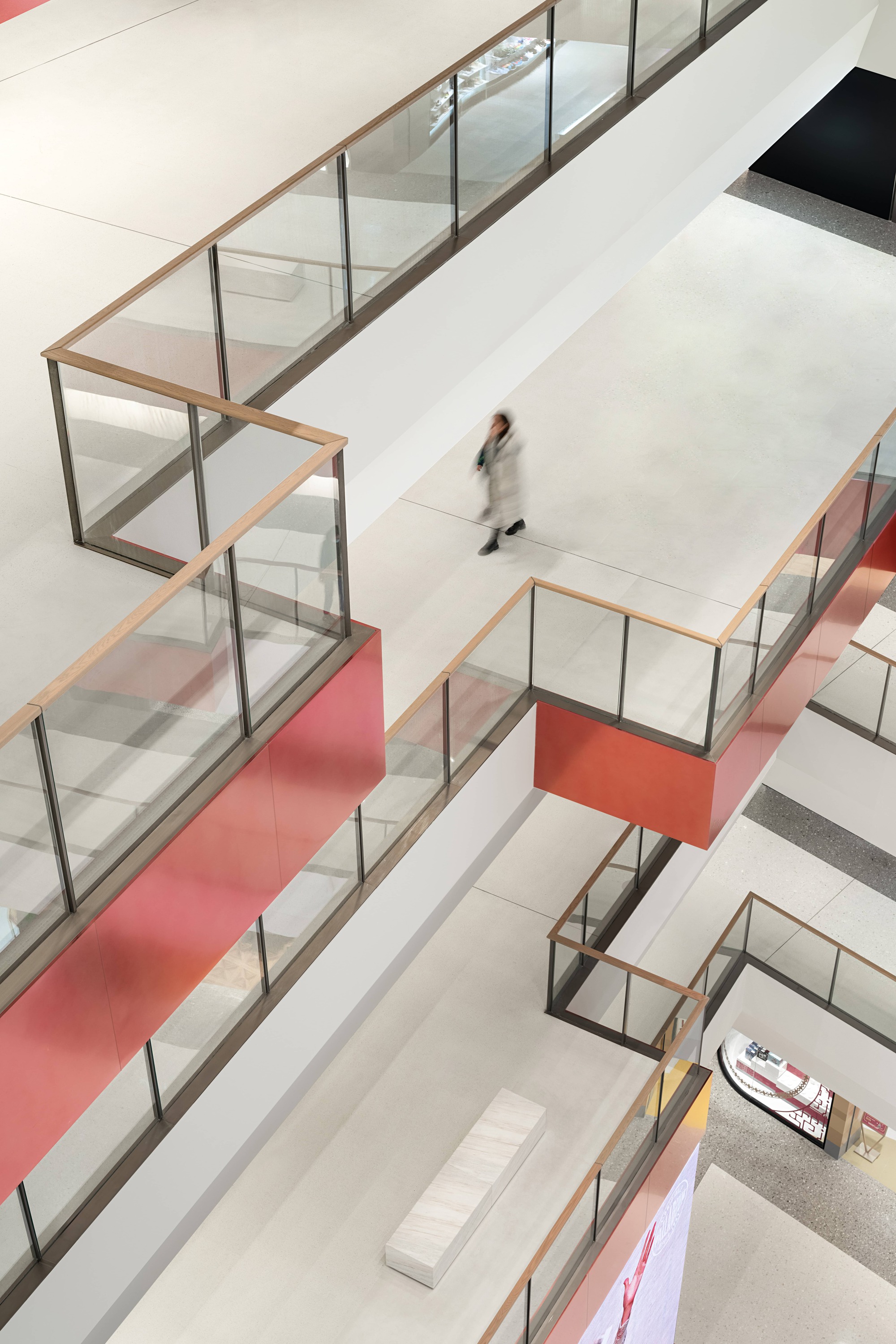 Overhead view of glass-railed display cases with red accent bands and a visitor walking below