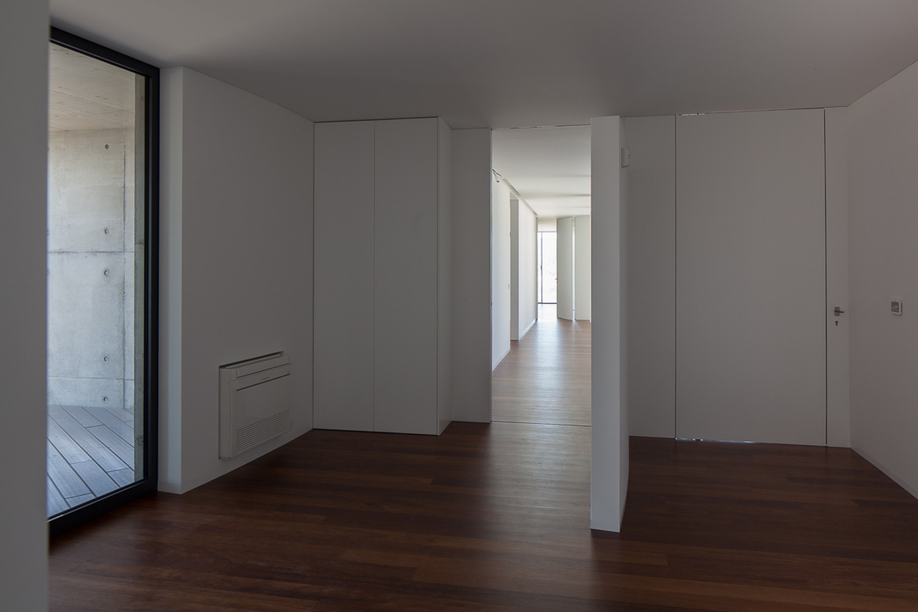 Room with white built-in cabinets and dark timber floor, a doorway leading to a long corridor and a glazed door at left