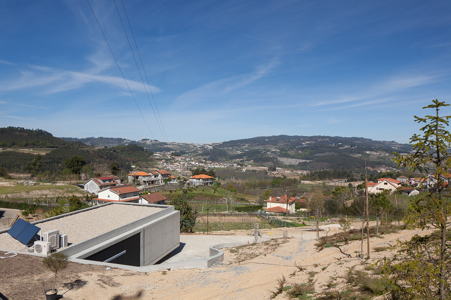 Gravel-topped concrete roof with solar panel and heat pumps, set on a hillside above a valley of red-roofed houses