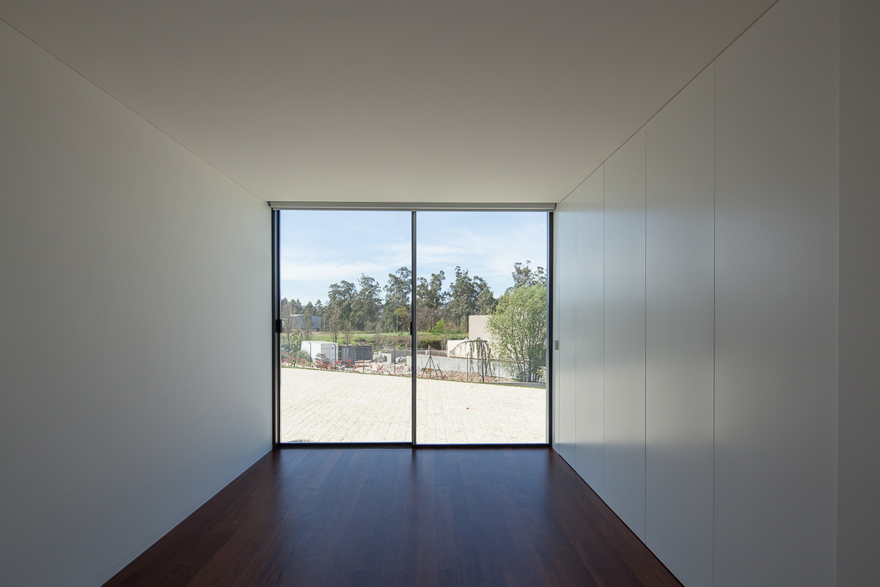 Bare room framed by white wardrobe panels and a sliding glass door looking out to a paved yard and eucalyptus trees